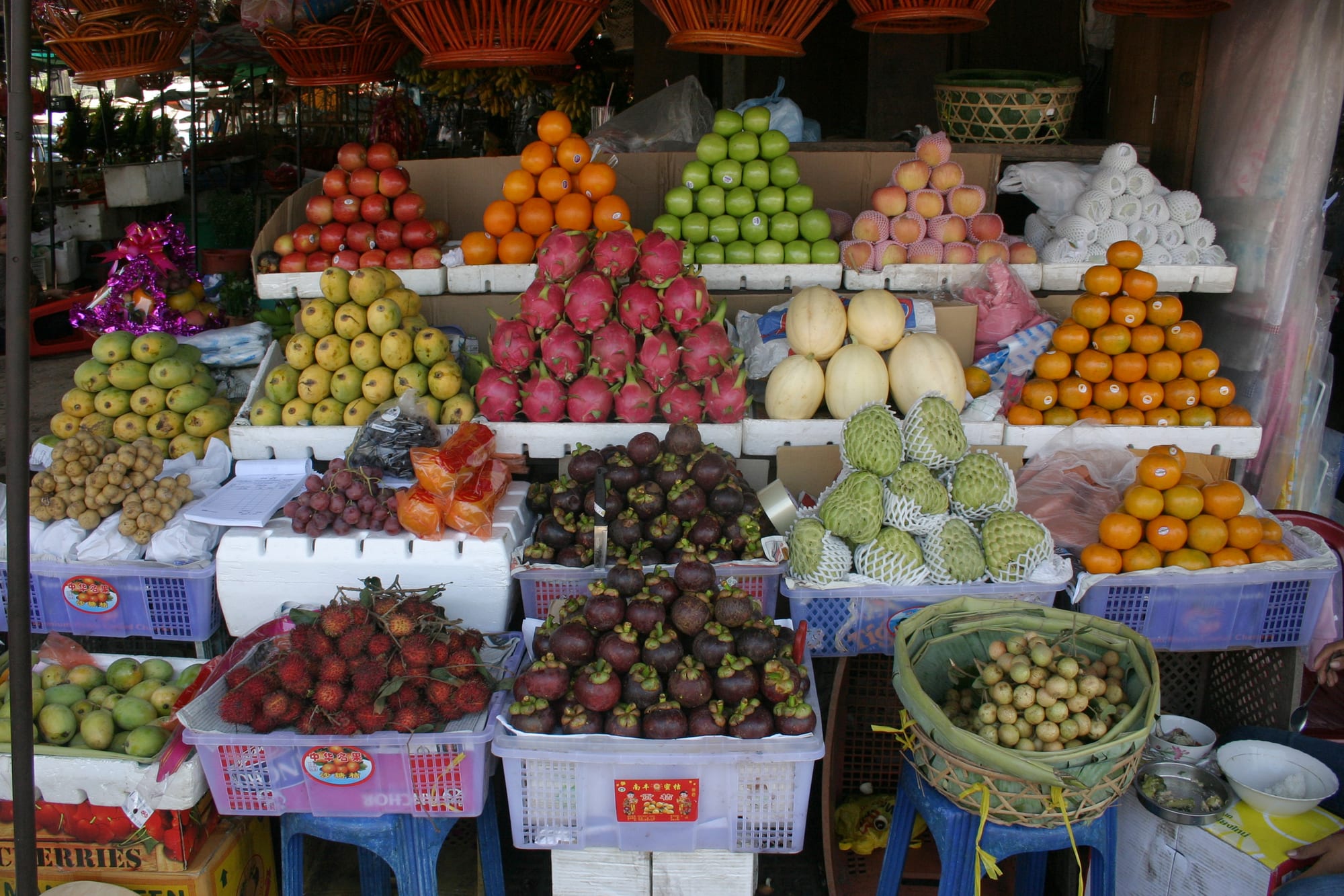 Neat pyramids of tropical fruit — apples, oranges, dragon fruit, rambutan, mangosteen — stacked on a market stall