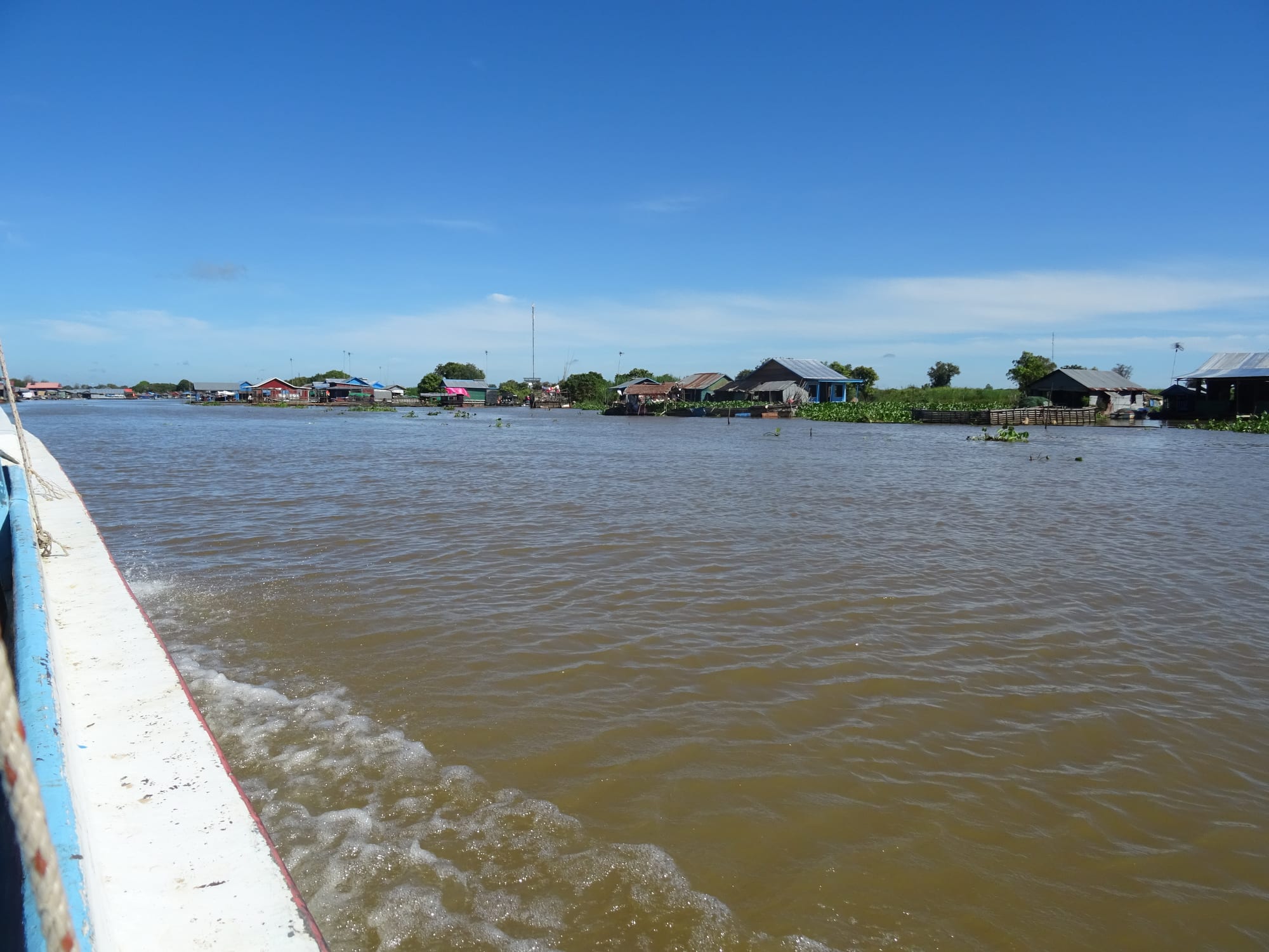 Wooden houses on tall stilts and floating platforms along a muddy river channel