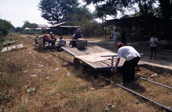 A flat bamboo platform on train wheels carrying passengers along a single rusty rail line