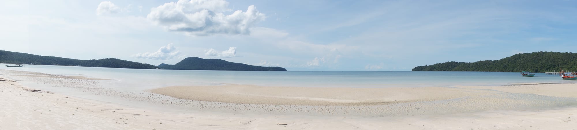A long crescent of white sand and clear shallow water backed by jungle, wooden jetties