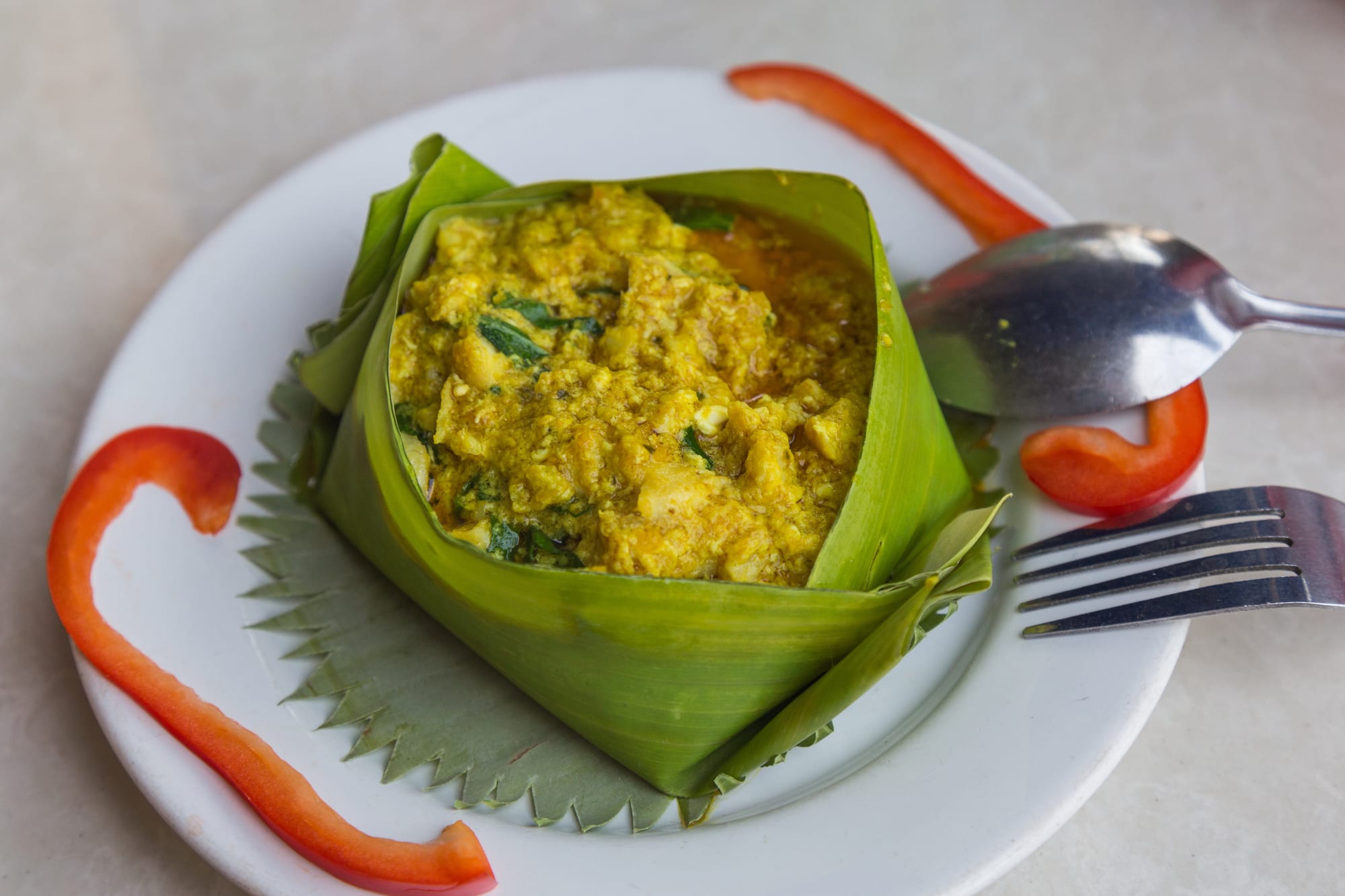 A small bowl of pale orange, custard-like fish curry topped with coconut cream and herbs