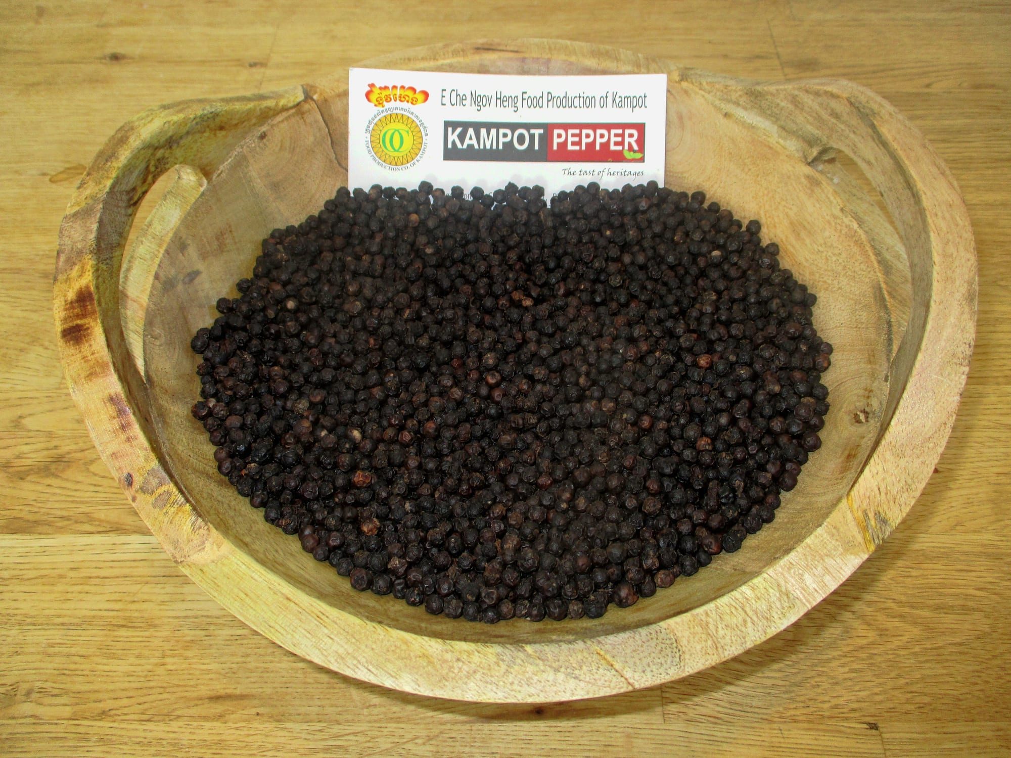 A wooden bowl filled with dried black peppercorns