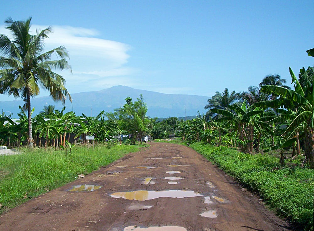 A broad volcanic mountain rising from lowland plantations, its summit under cloud