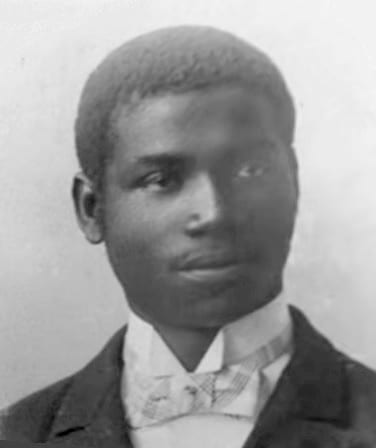 A formal early 1900s portrait photograph of a Douala king in a dark European-style suit