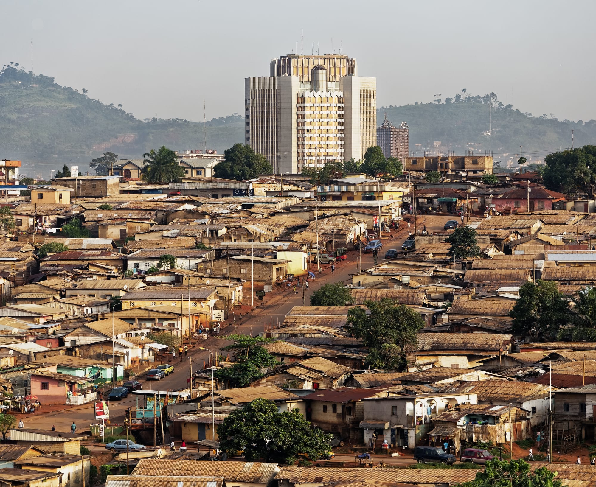 A tall modern glass tower and government buildings on a green hillside in a large African city