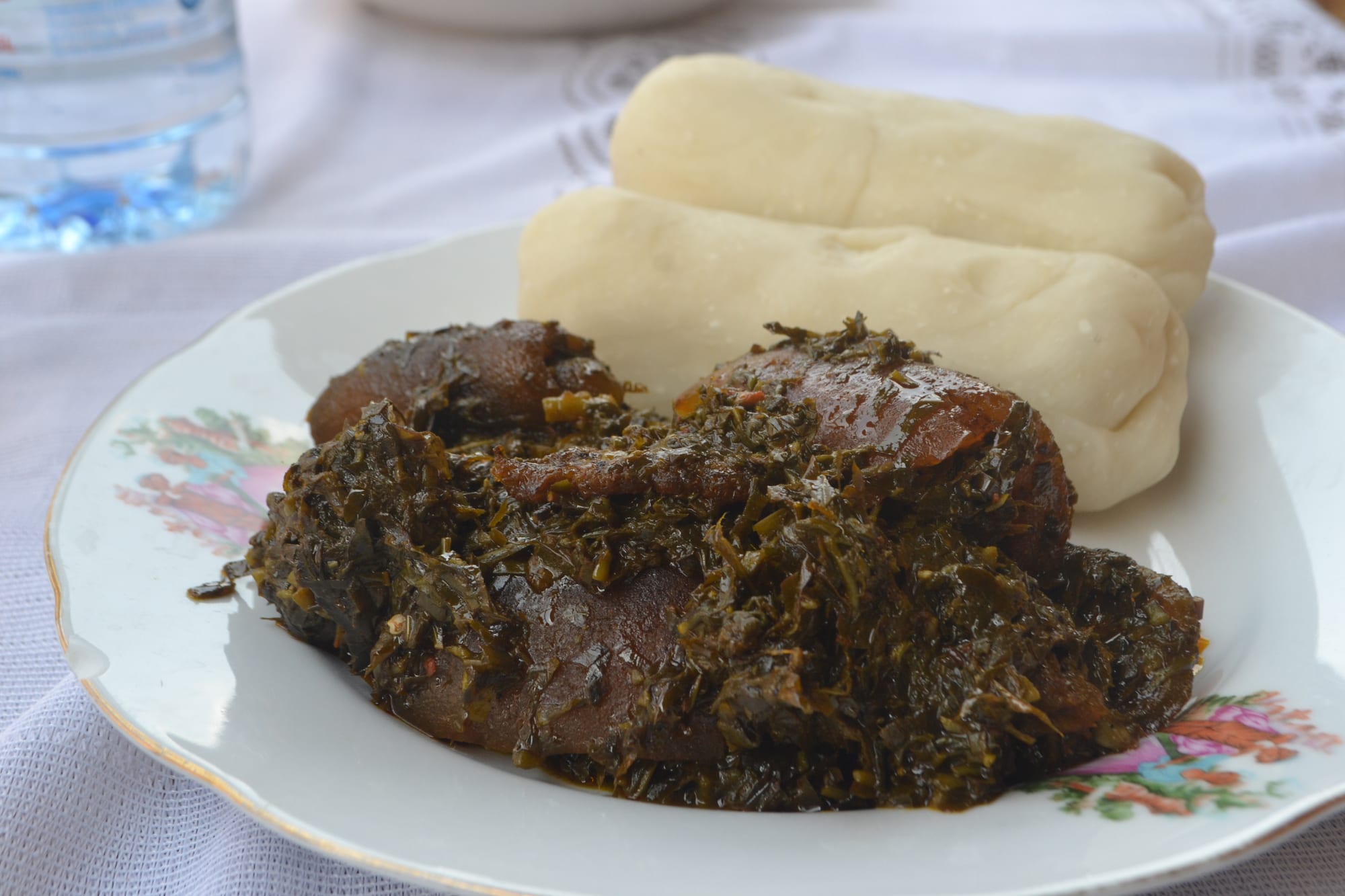 A plate of dark green shredded leaf stew beside a pale, smooth starch paste