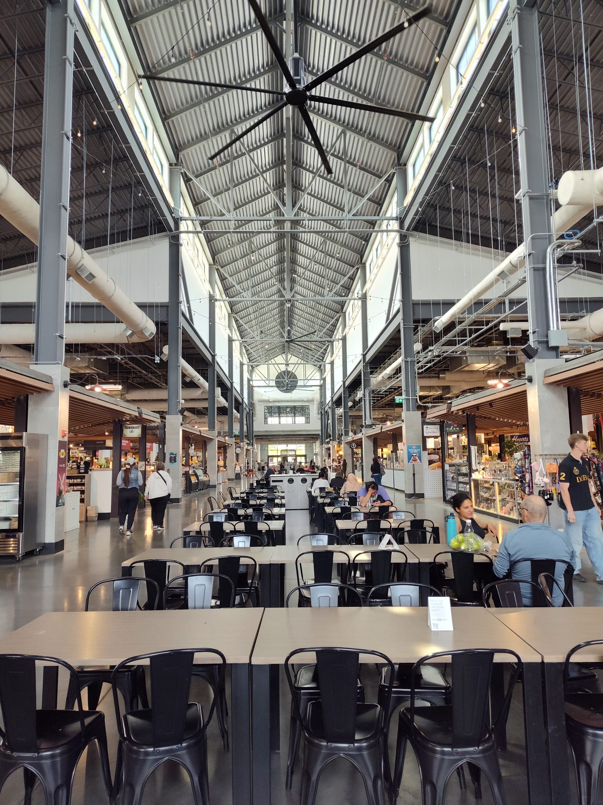 The high, steel-raftered interior of an indoor market hall lined with food stalls and communal seating