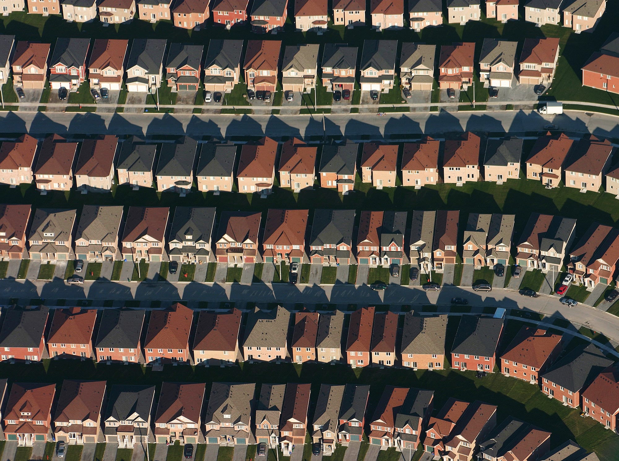 Aerial view of curving suburban streets lined with rows of similar detached houses, each with a driveway and small garden