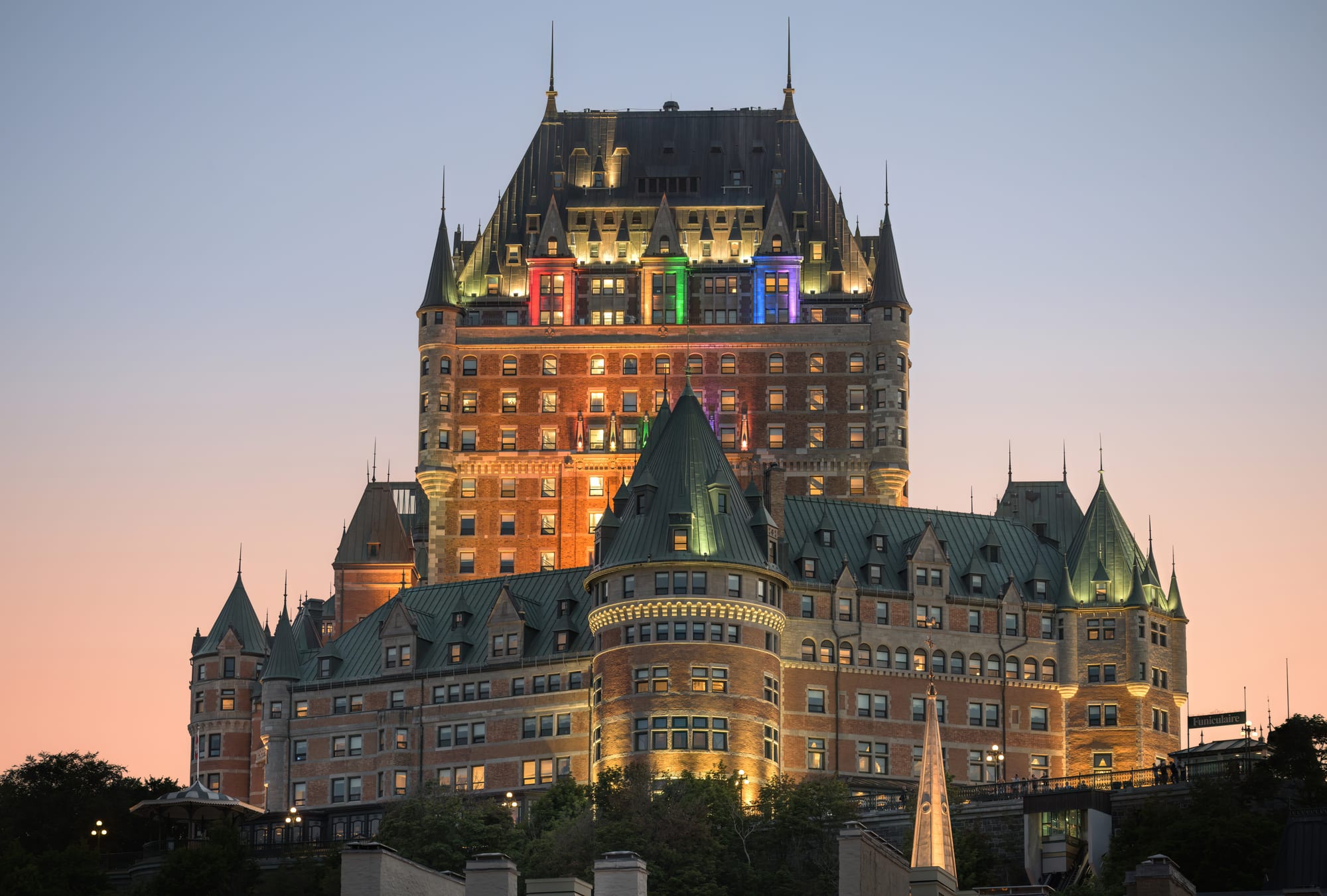 A huge green-roofed château-style hotel on a cliff above a river at dusk