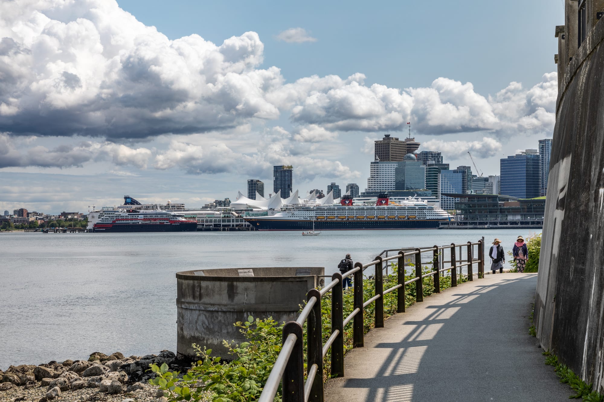 A waterfront path curving around a forested peninsula with the city skyline and mountains beyond