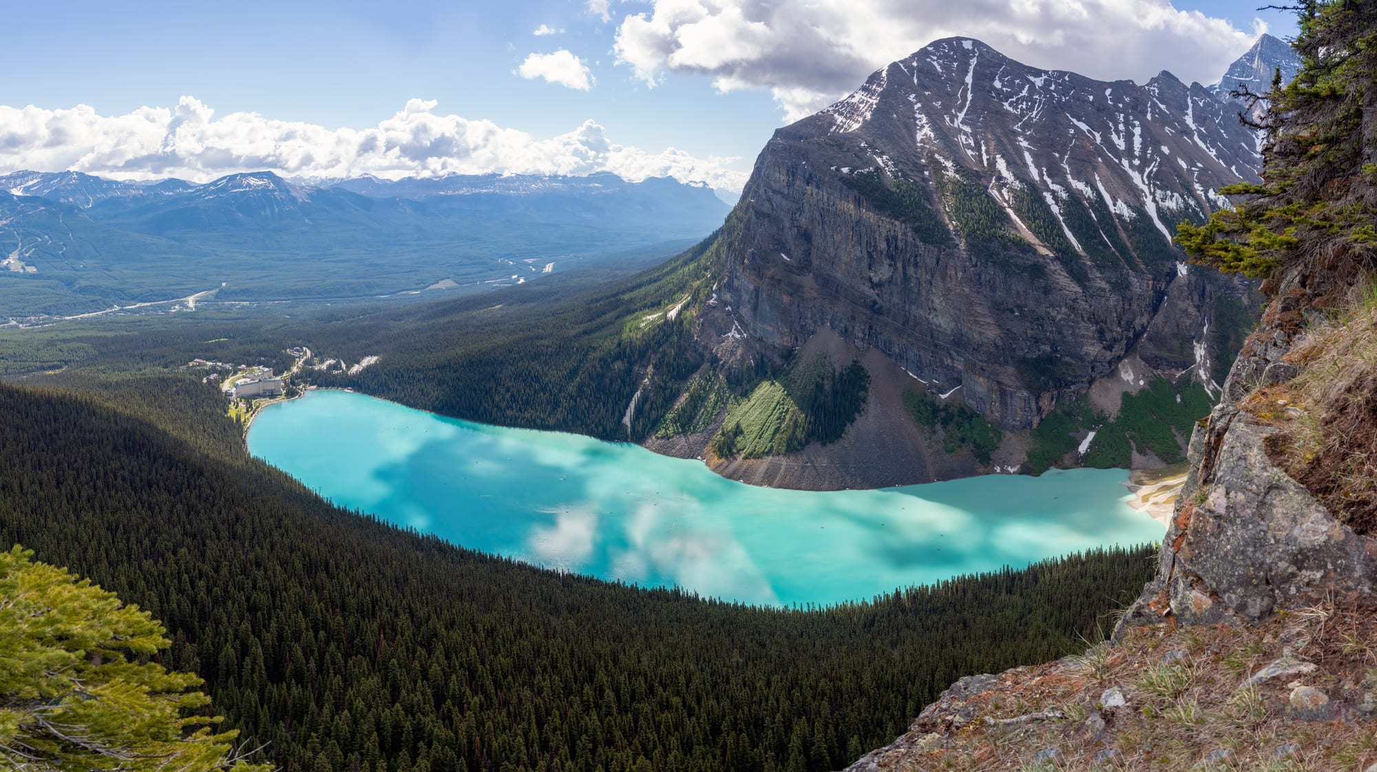 A green-blue lake leading the eye to a glacier between mountains, a grand hotel on the near shore