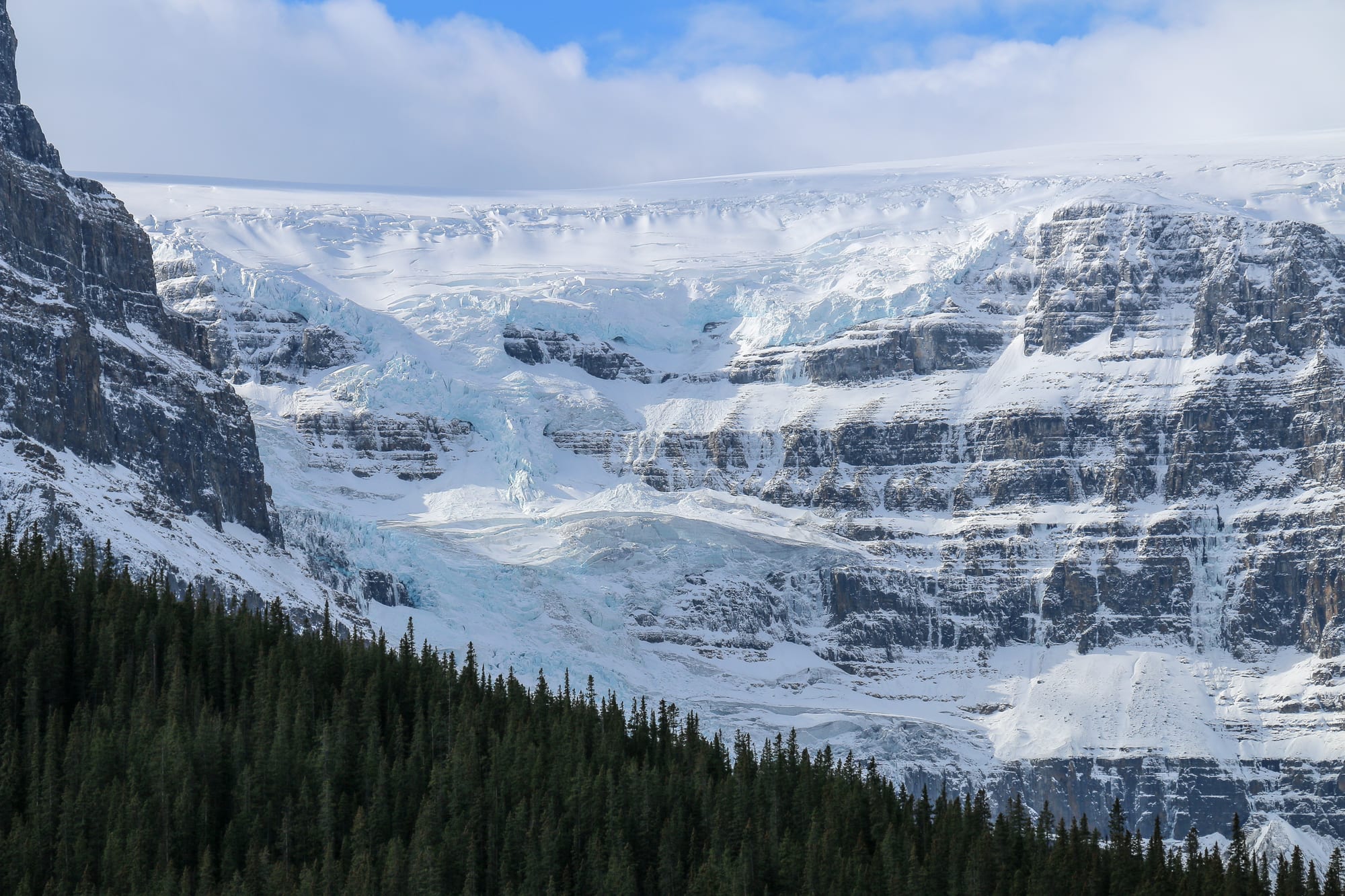 A highway running through a broad glacial valley between high snow peaks and forest