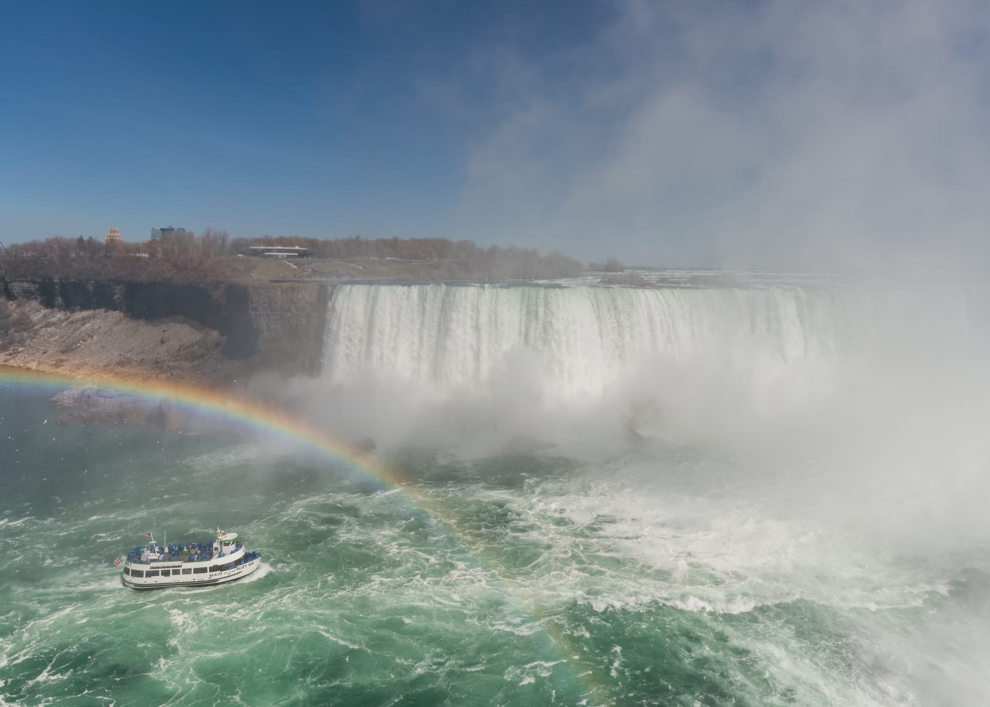 A tour boat dwarfed by a vast curving wall of falling water and mist