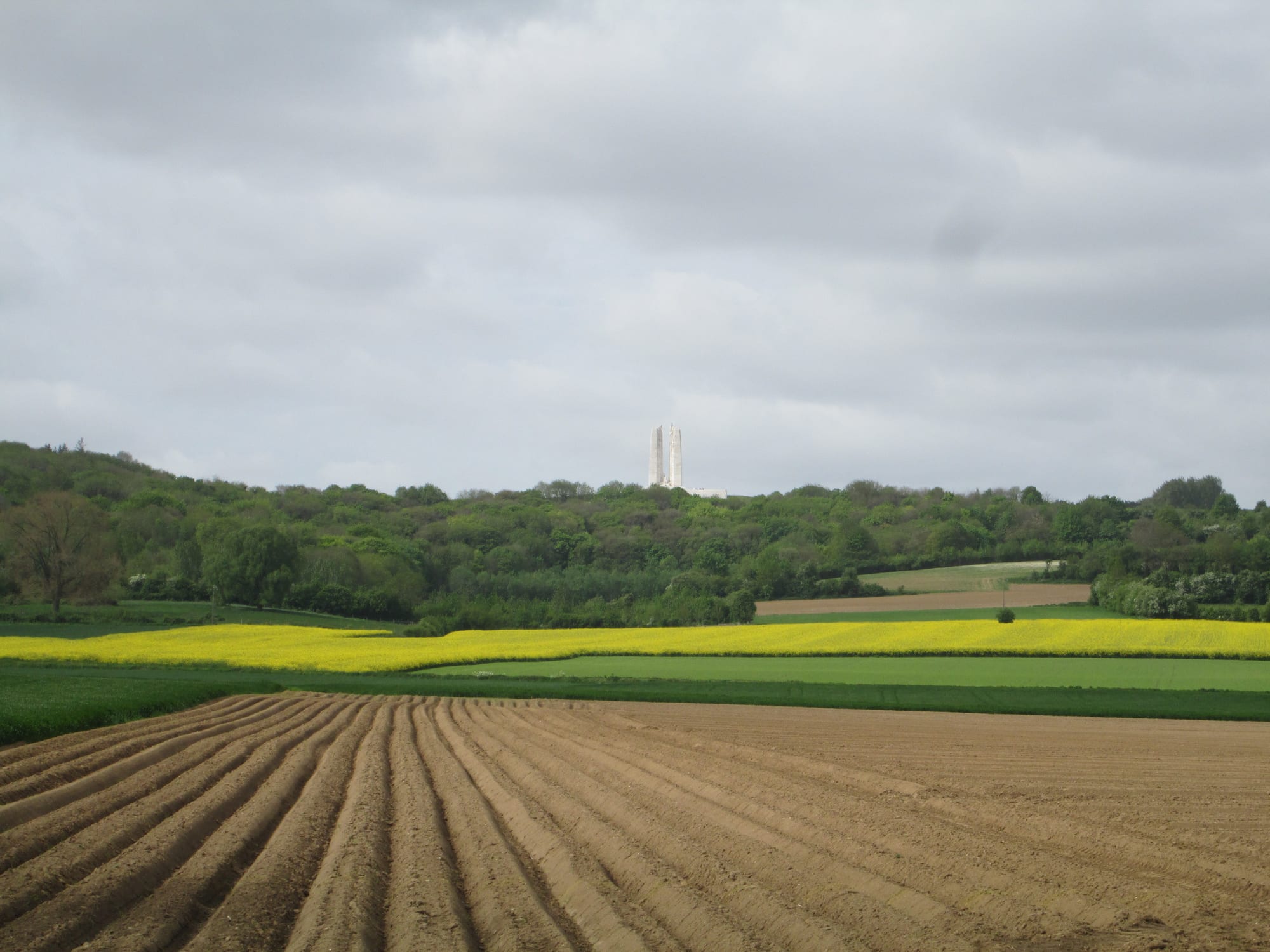 A towering white stone monument with two pylons and mourning figures, on a green ridge