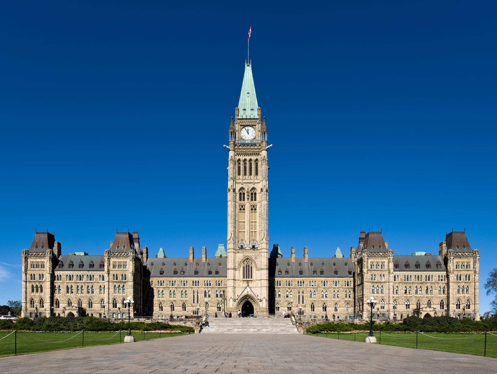 A Gothic Revival parliament building with a tall central clock-and-flag tower, on a hill
