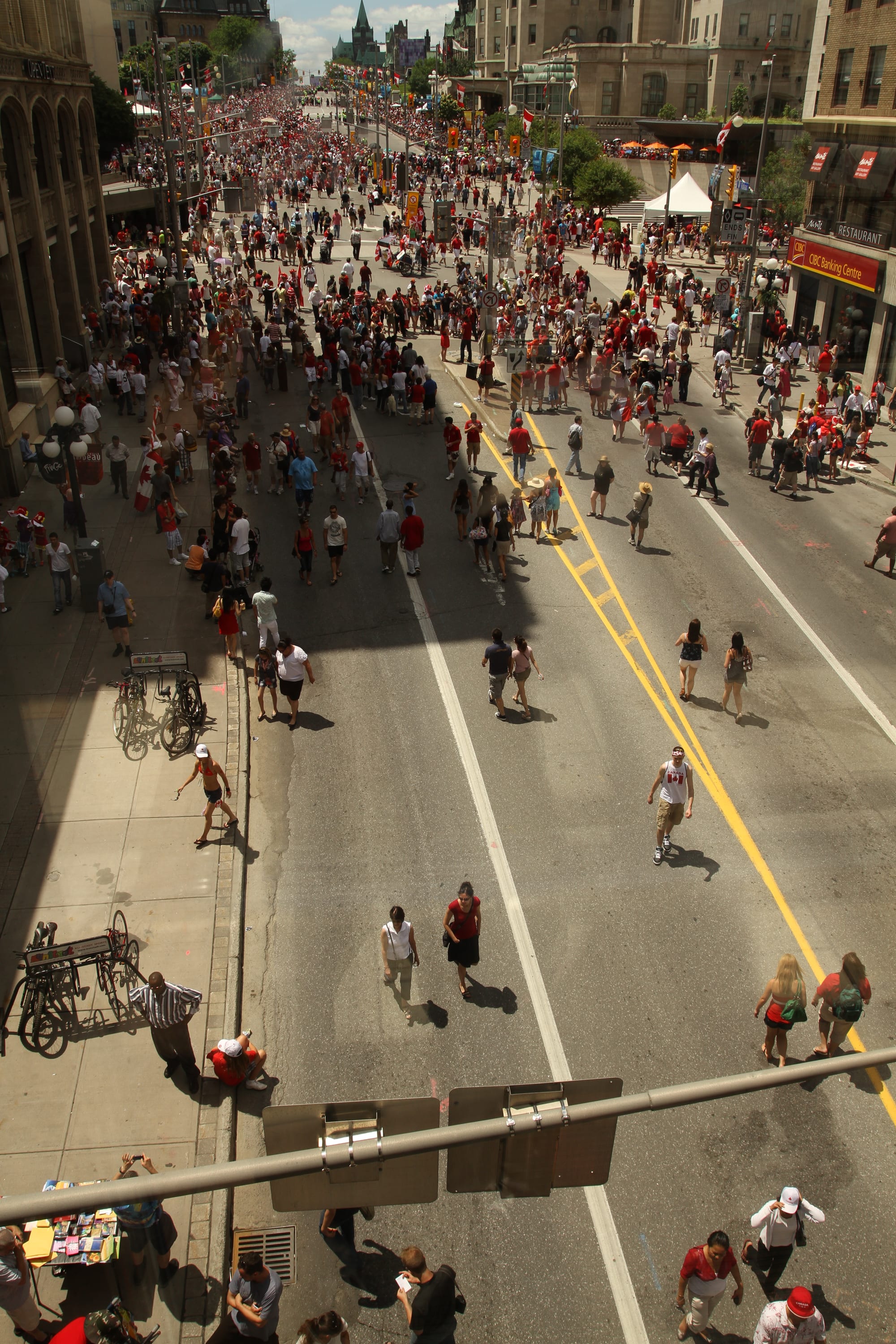 A wide city street closed to traffic and filled with crowds of people, many dressed in red and white, stretching into the distance between stone buildings