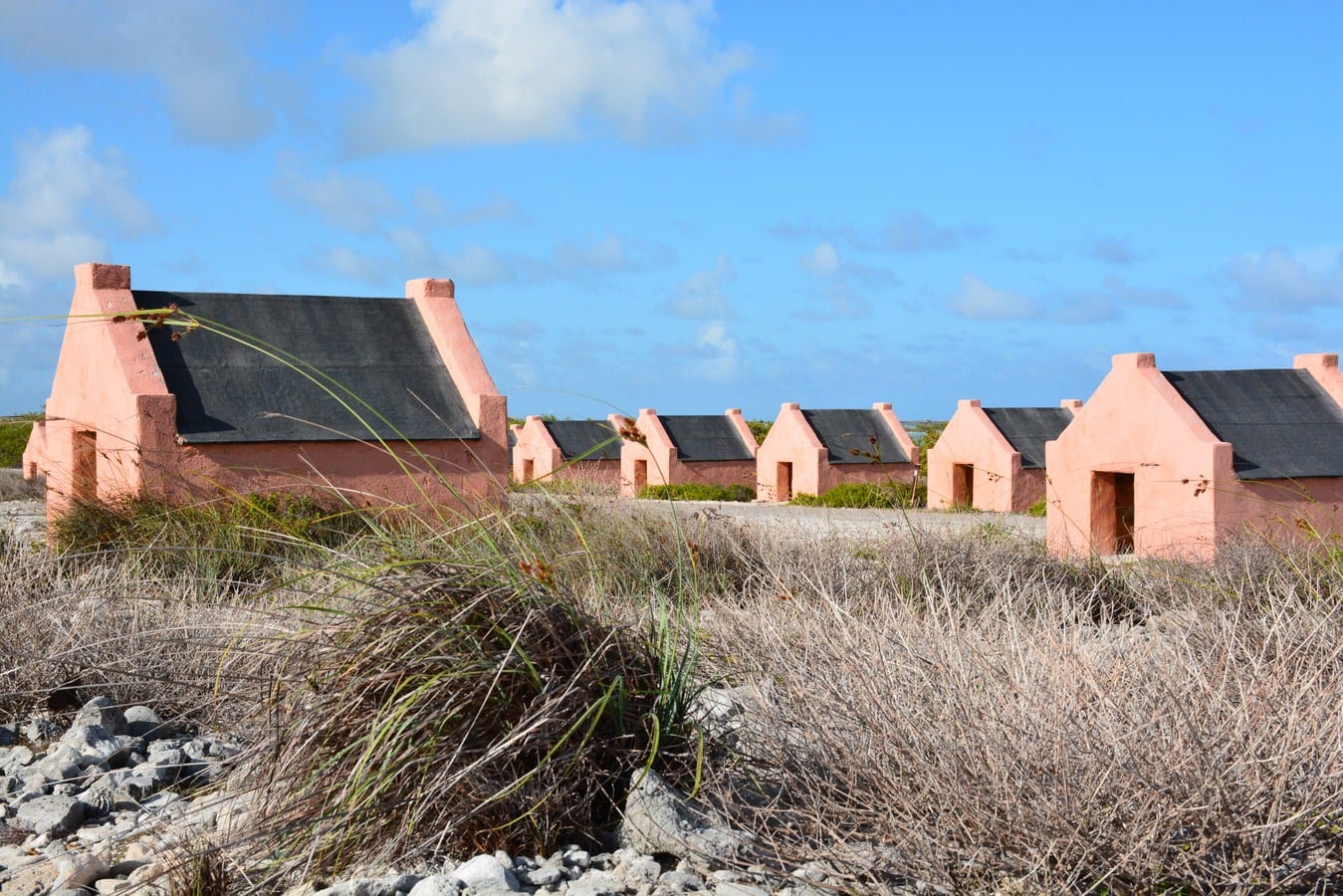 A row of tiny pink stone huts with peaked roofs on a bare stony coast in southern Bonaire