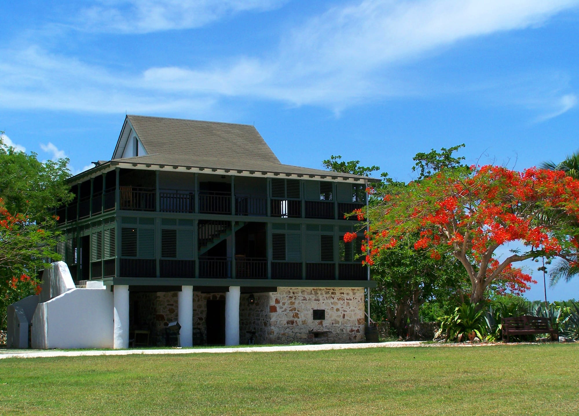 A three-storey stone-and-timber great house with wide verandas, on a low cliff above the sea