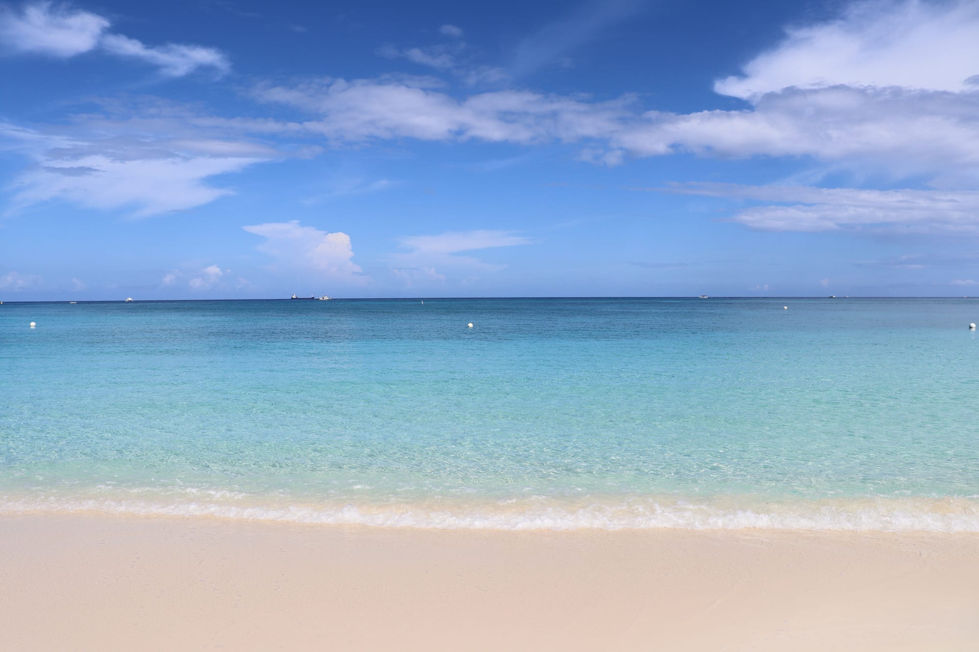 Calm clear shallows over white sand fading to deep blue, a few beach umbrellas