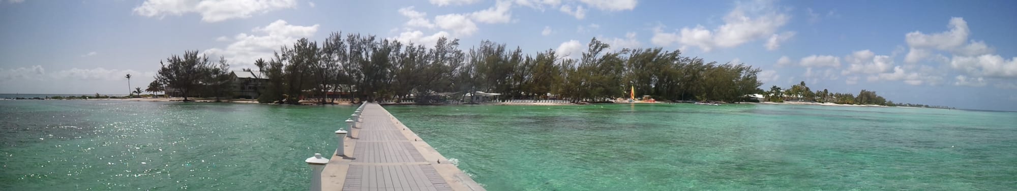 A shady palm-lined beach with hammocks and calm shallow water on a sand spit
