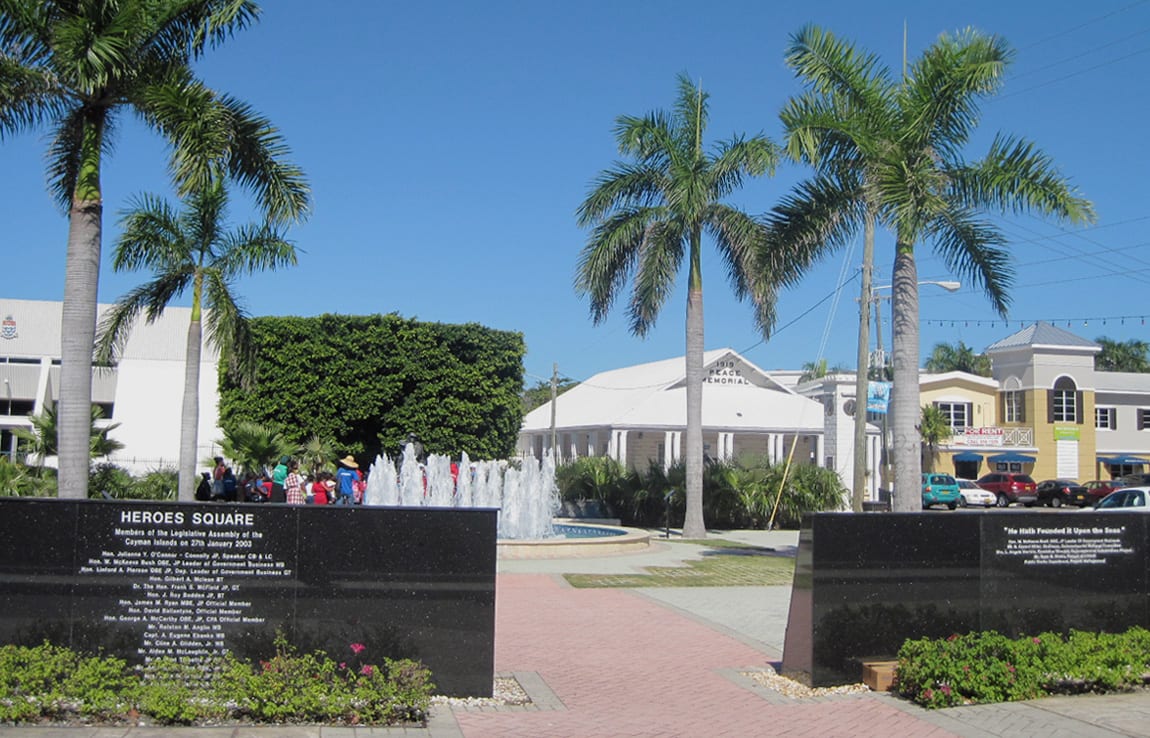 Heroes Square in George Town, with a fountain, memorial monuments, and the white Peace Memorial building framed by tall royal palms