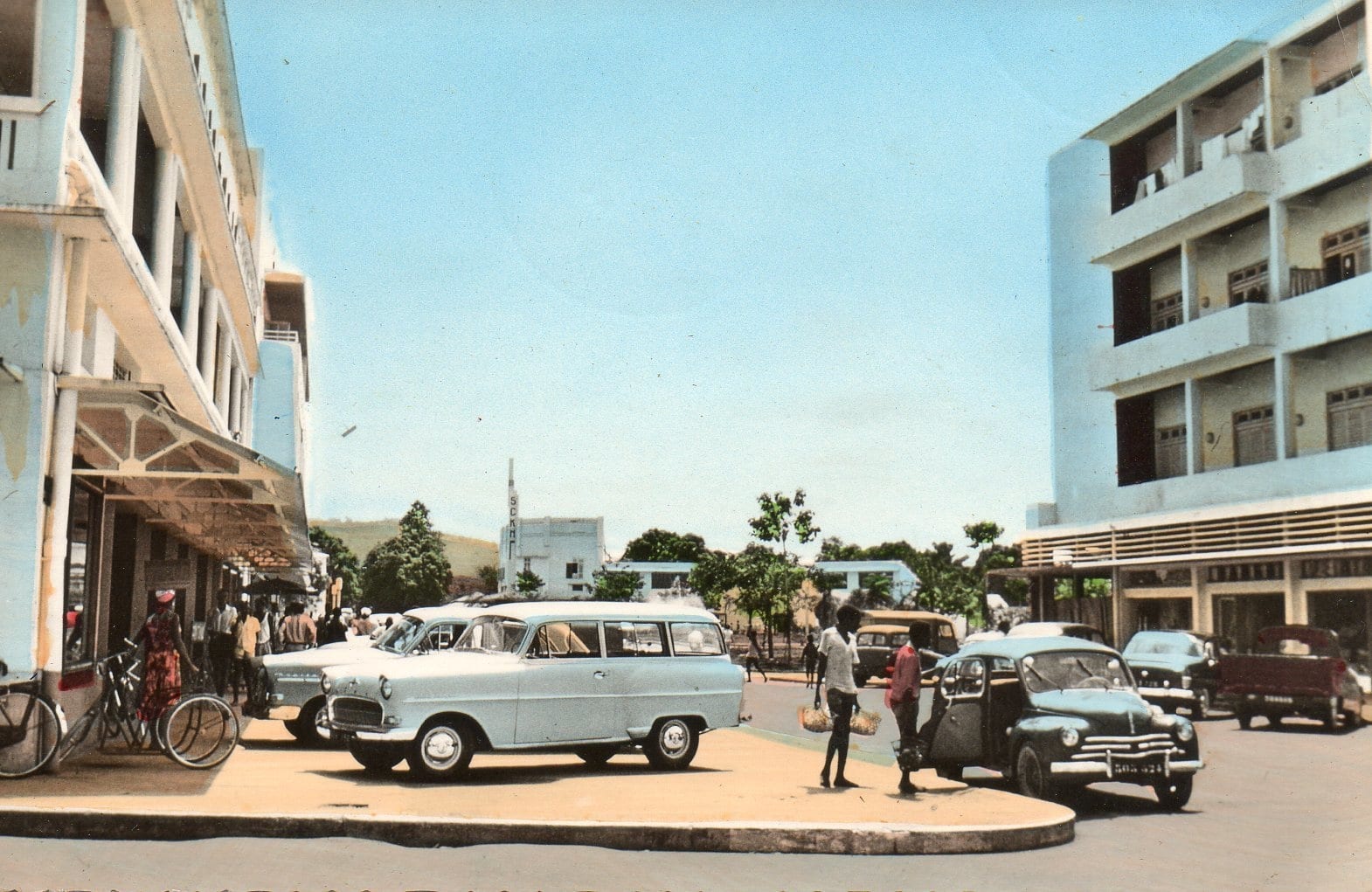 A 1960 street scene of a low colonial town with a church, palms and a few cars