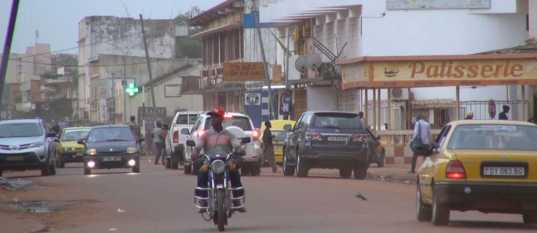 A busy Bangui street with motorbikes, minibuses and pedestrians under a hazy sky