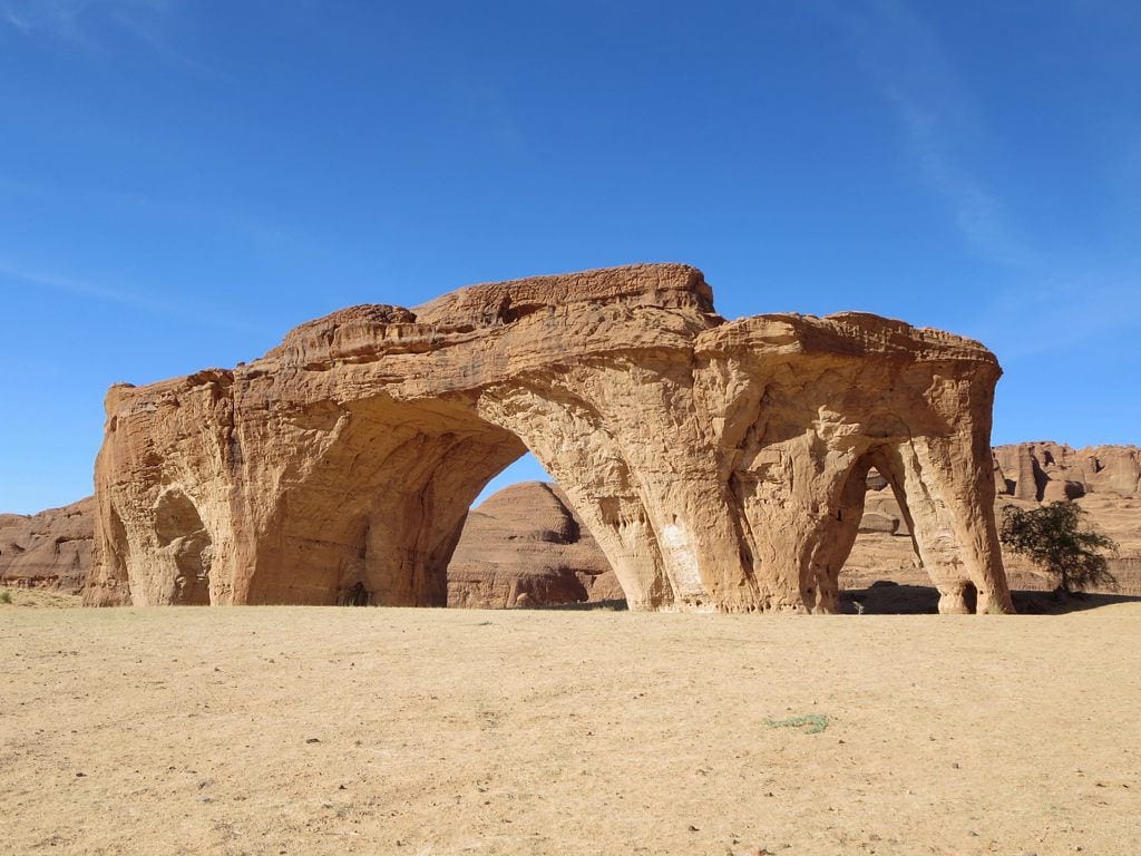 A sandstone outcrop pierced by several natural arches, standing in open desert