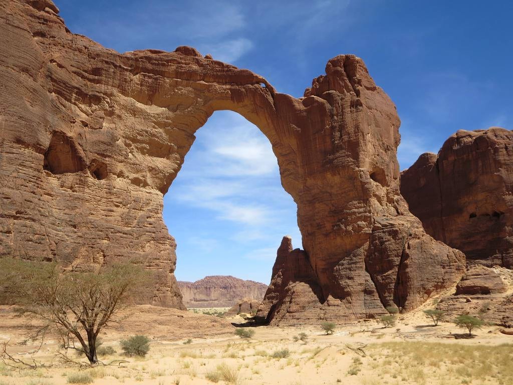 An enormous natural sandstone arch, hundreds of metres tall, spanning a bare desert gorge