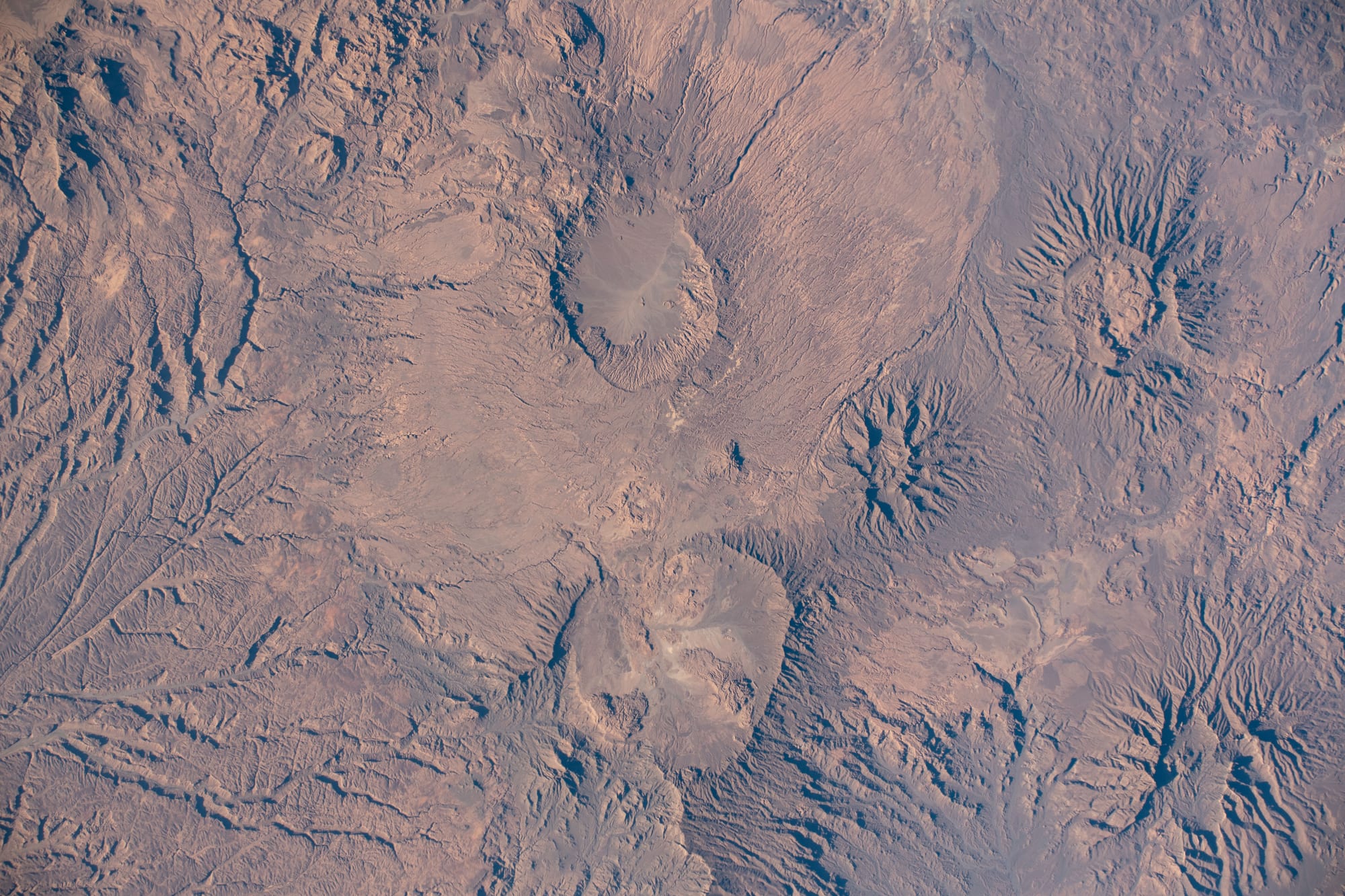 A dark volcanic mountain range with craters and lava flows, seen from orbit