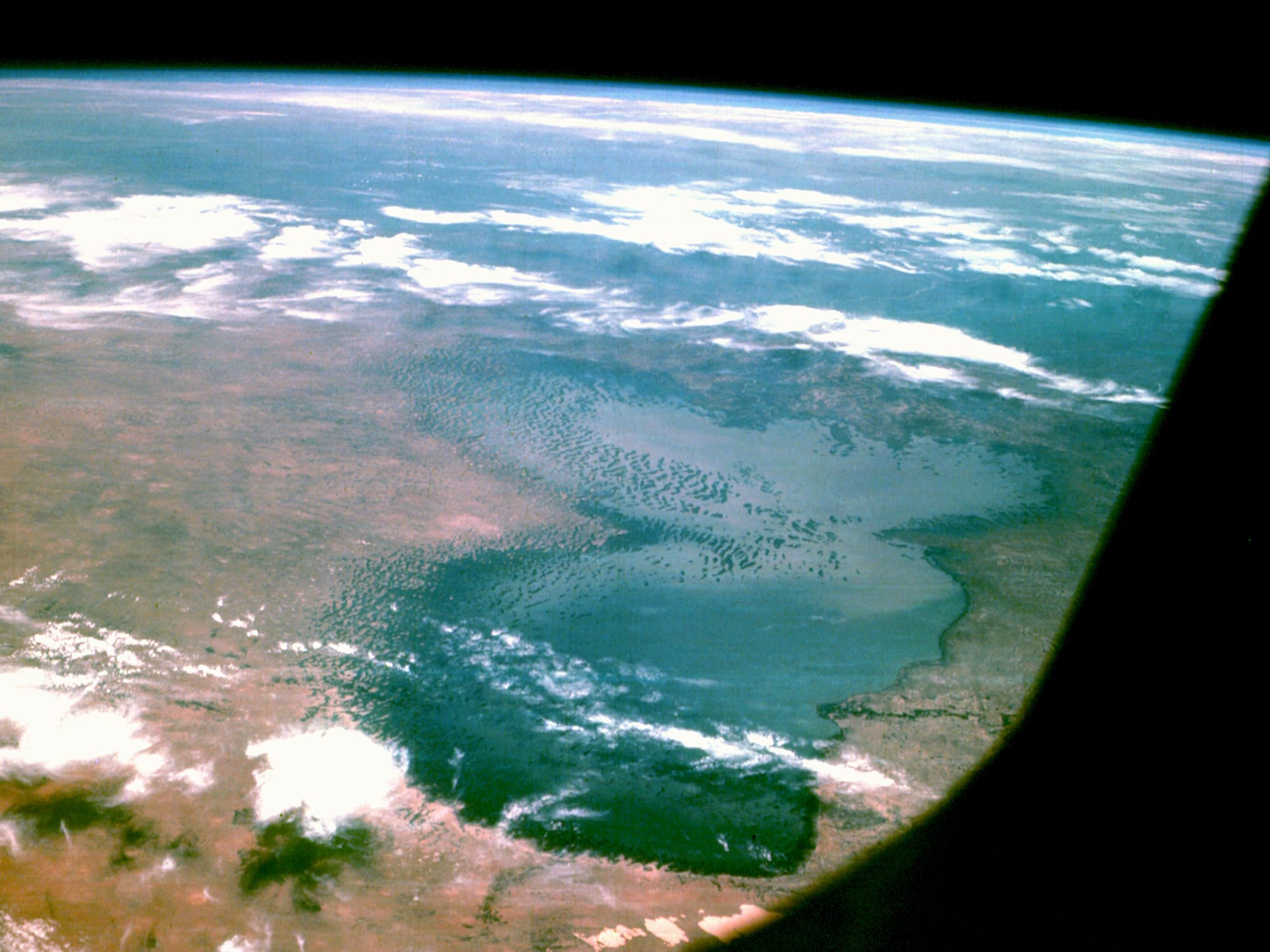 A satellite view of a large shallow lake fringed with green, surrounded by pale desert