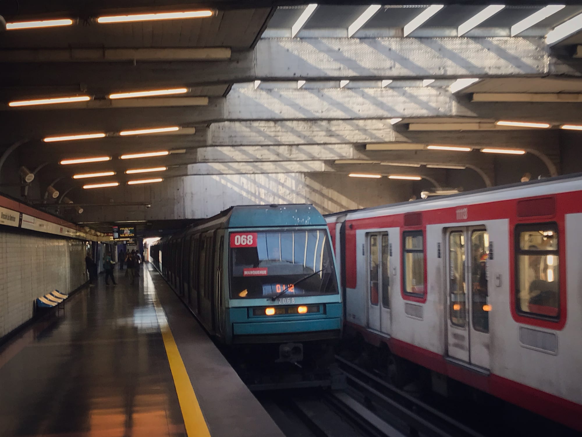 Two Santiago Metro trains, one turquoise and one white and red, stopped at an underground platform