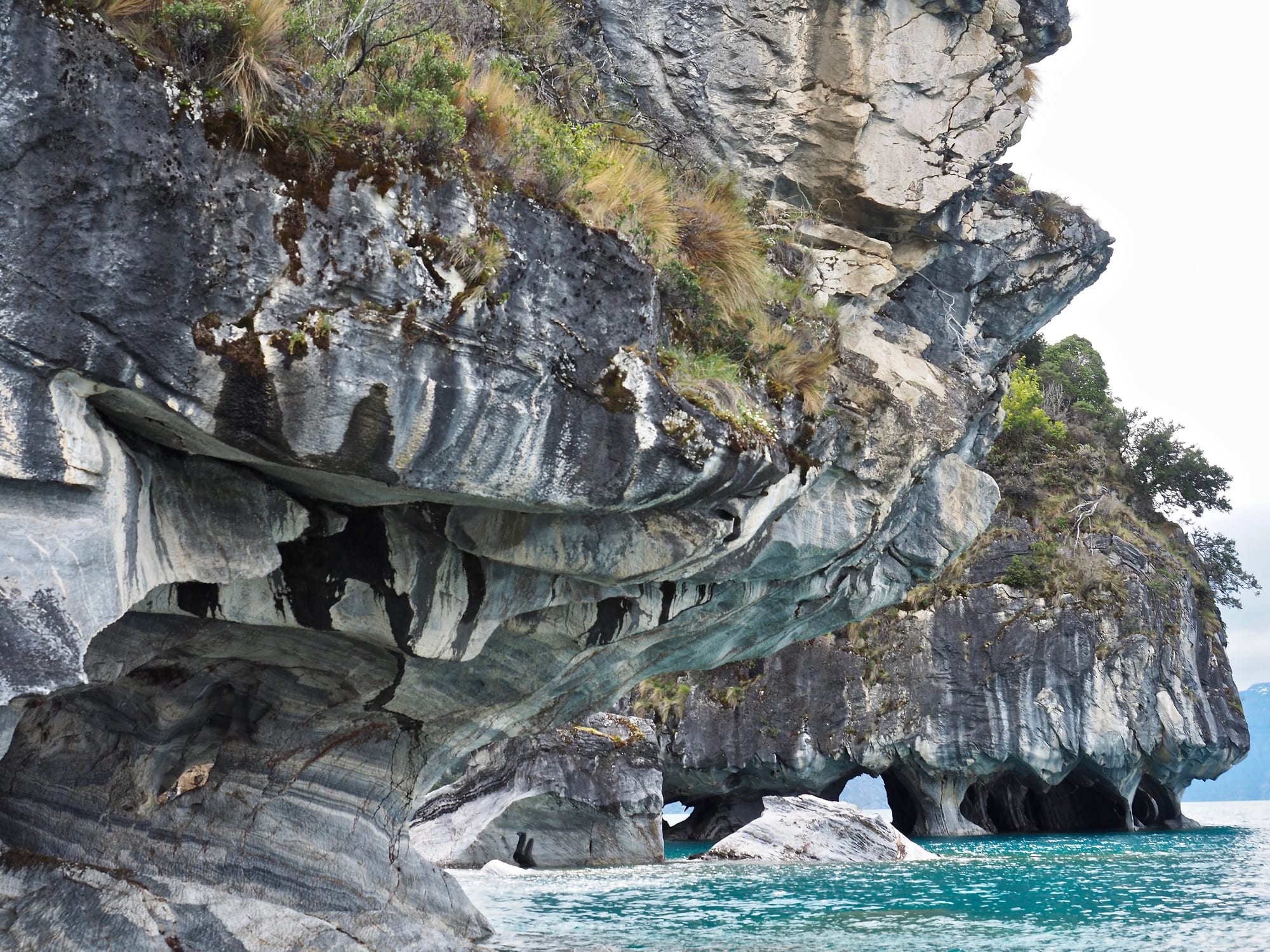 Swirling banded marble walls and columns rising from vivid blue water inside a cave