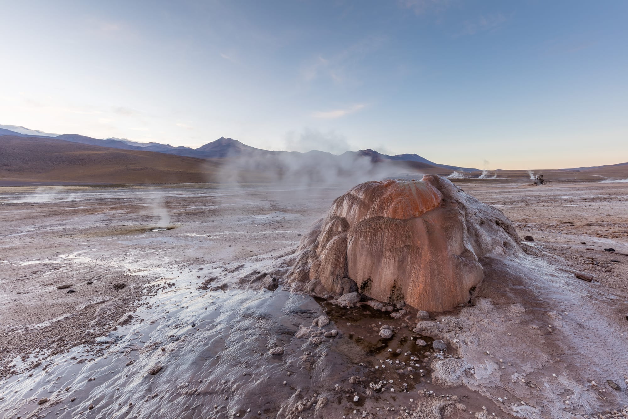Columns of steam rising from a geyser field on a high desert plain at dawn