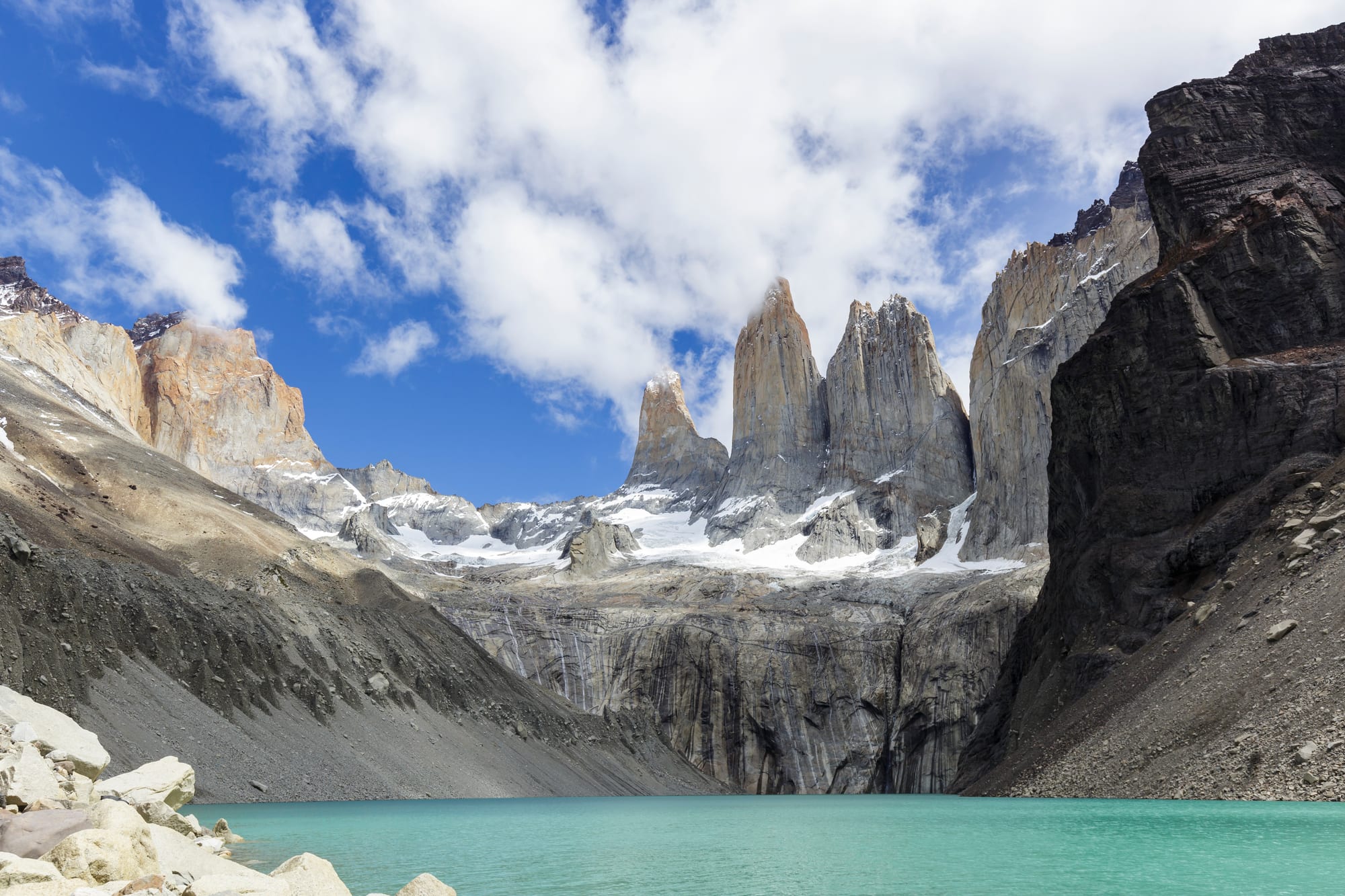 Three sheer granite spires catching sunrise light above a turquoise glacial lake
