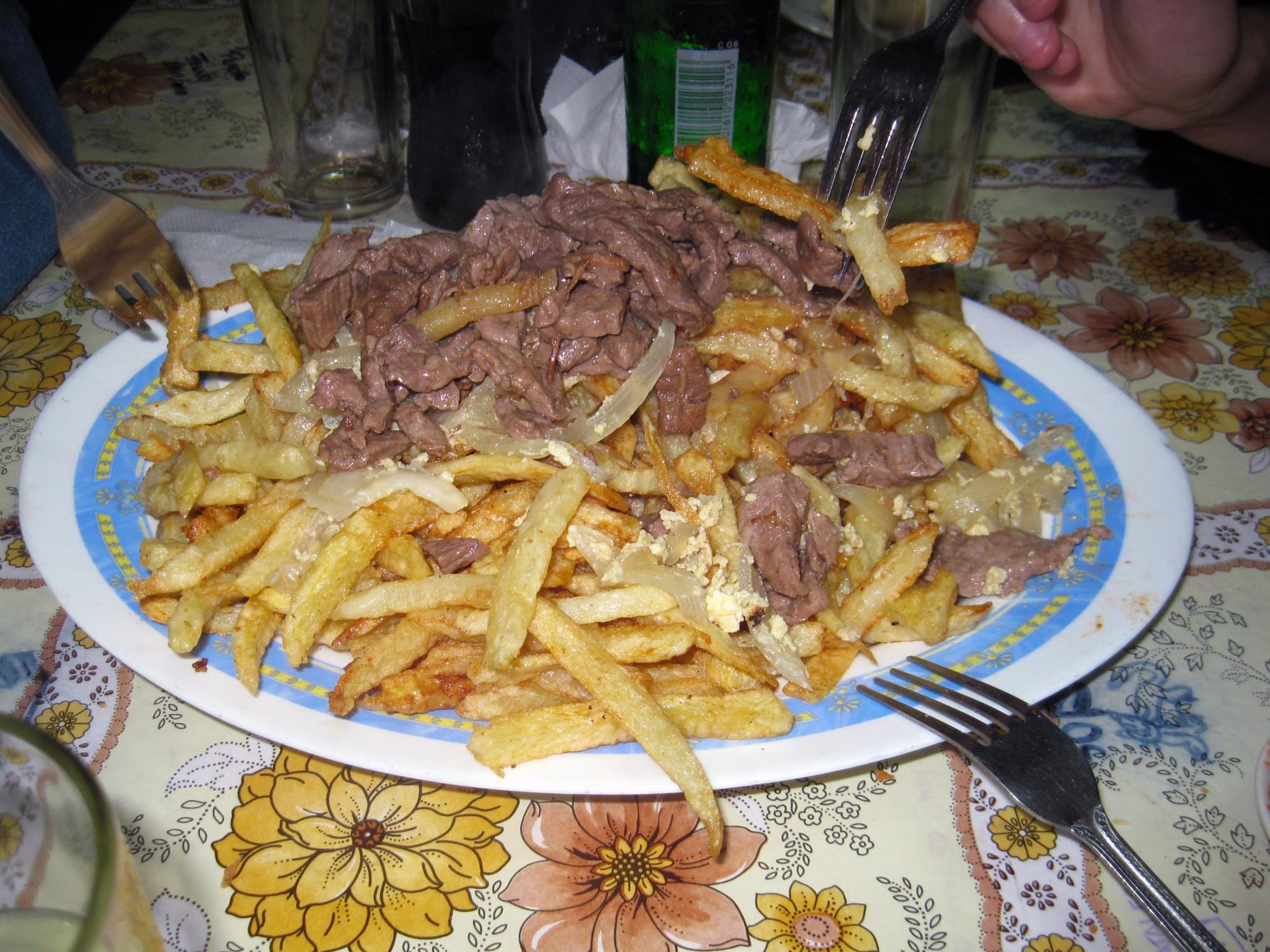 A large plate piled with fries, fried egg, onion and meat