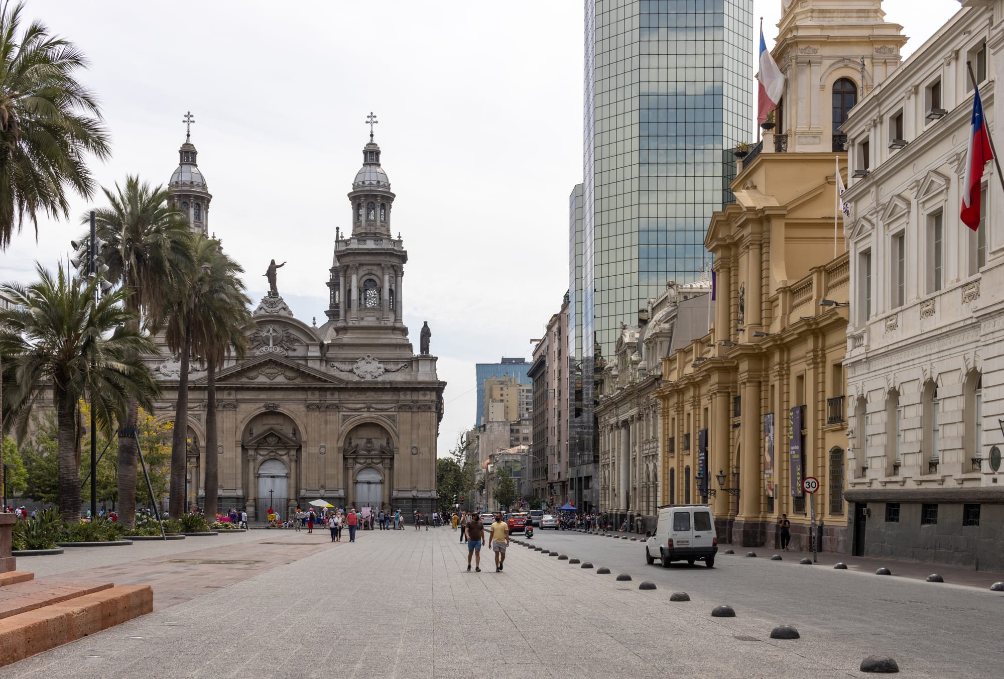 A large neoclassical stone cathedral with twin towers facing a palm-lined city square