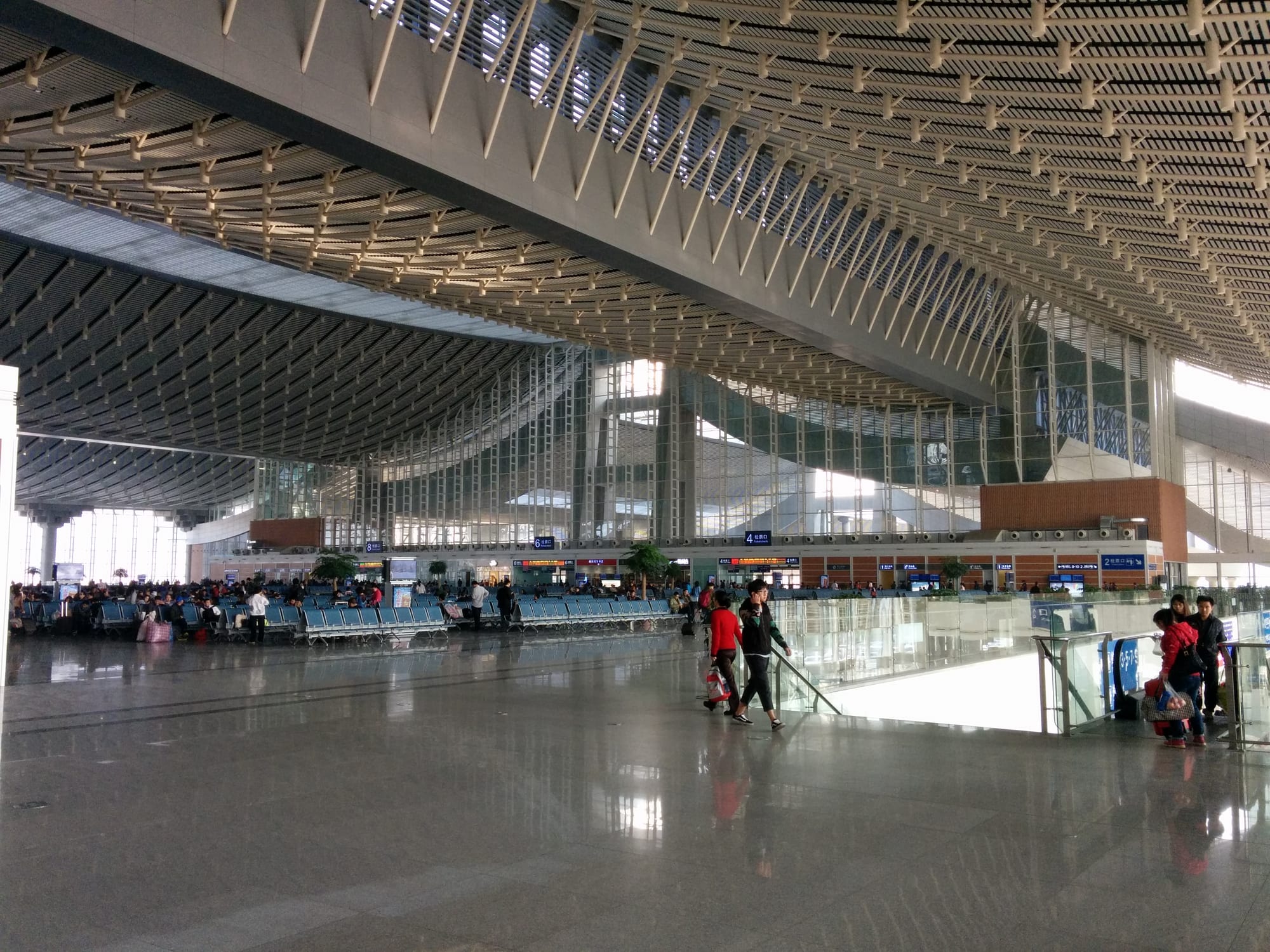 A vast, light-filled modern railway station departure hall with rows of seating and passengers walking through