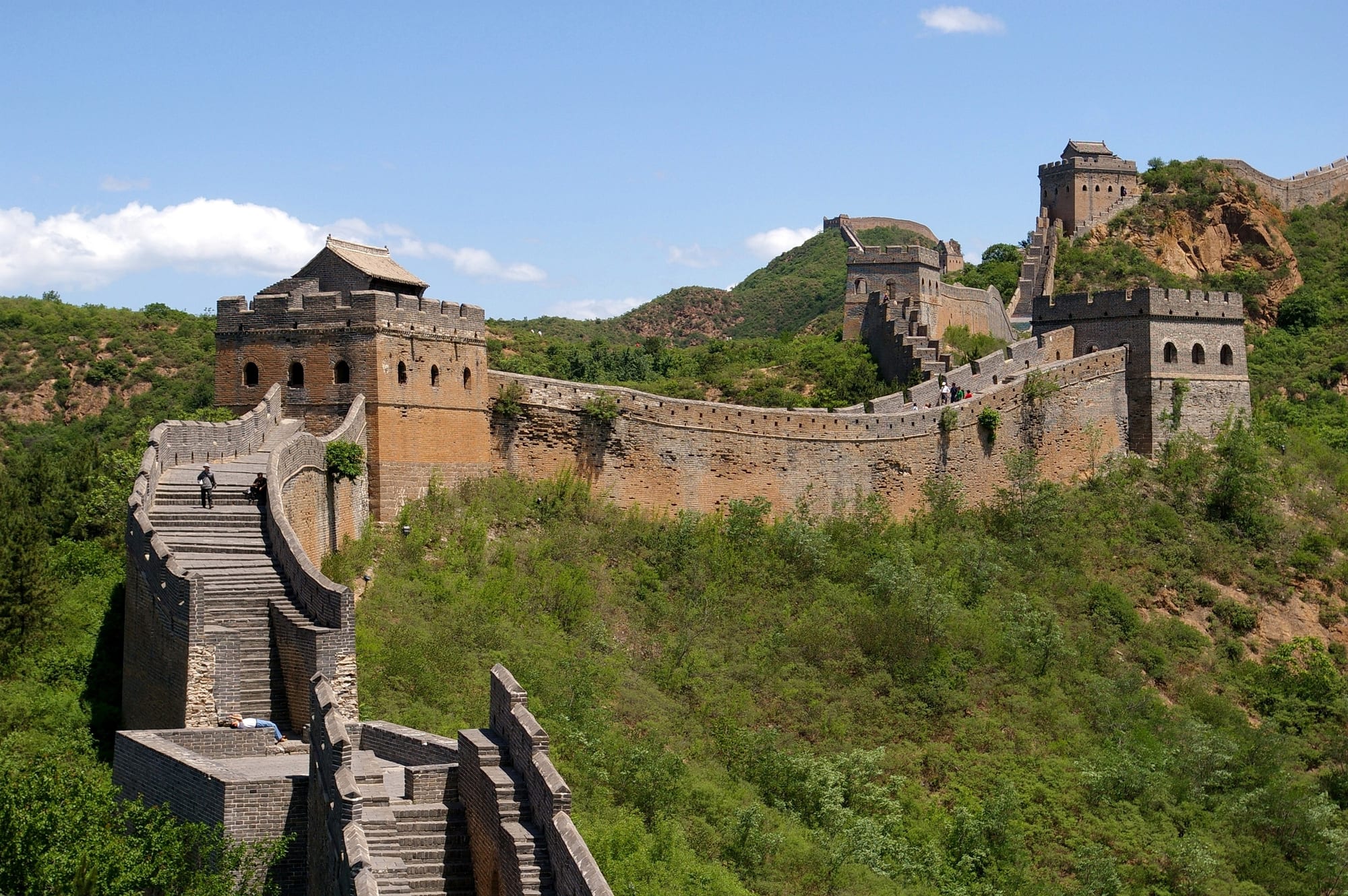 A stone wall with watchtowers snaking along the crest of steep forested mountain ridges