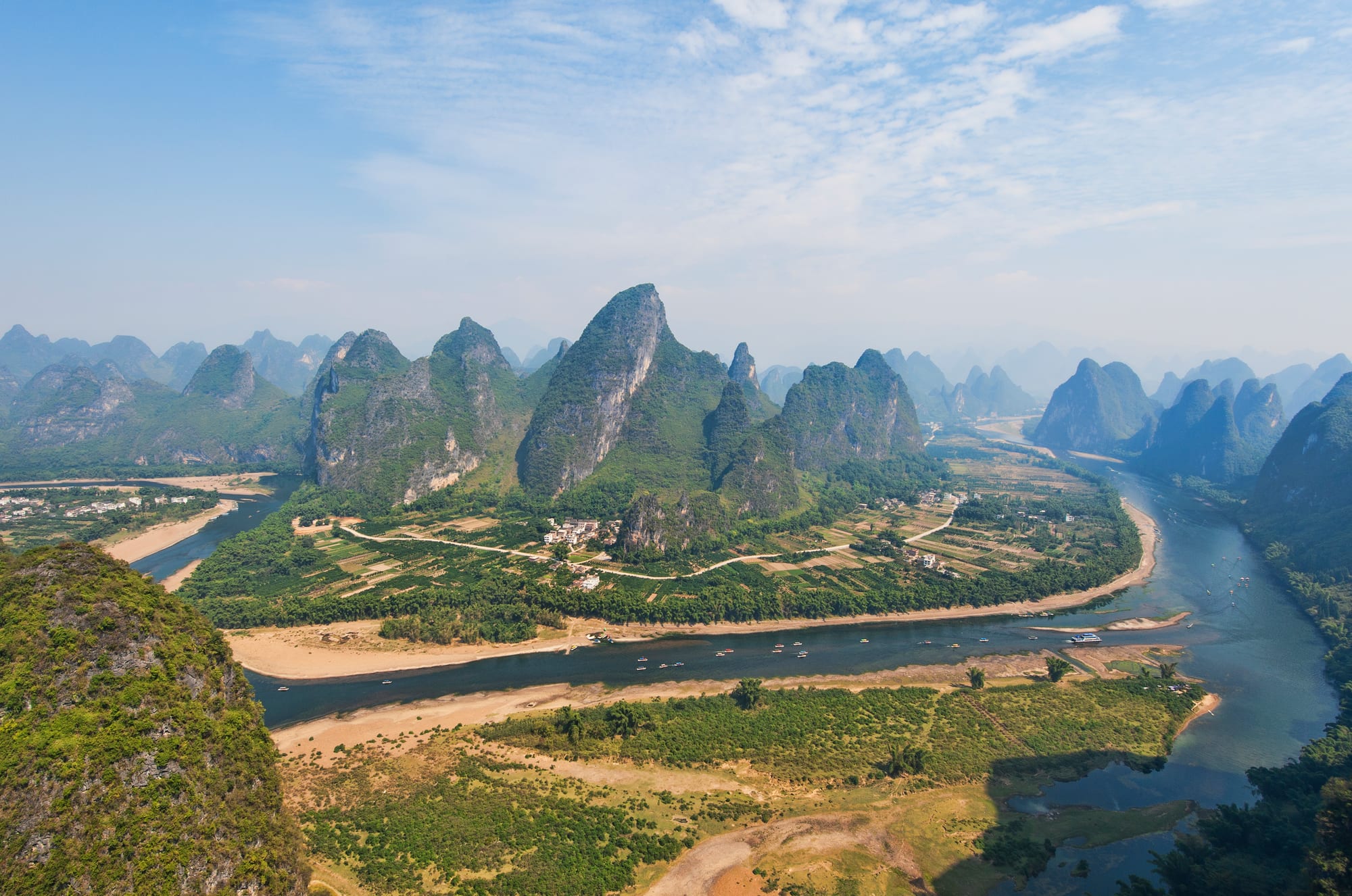 Steep isolated limestone peaks rising from a plain, a green river winding among them