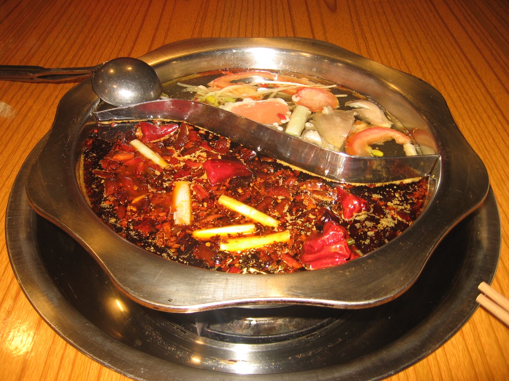 A large simmering pot of dark red, oily chilli broth