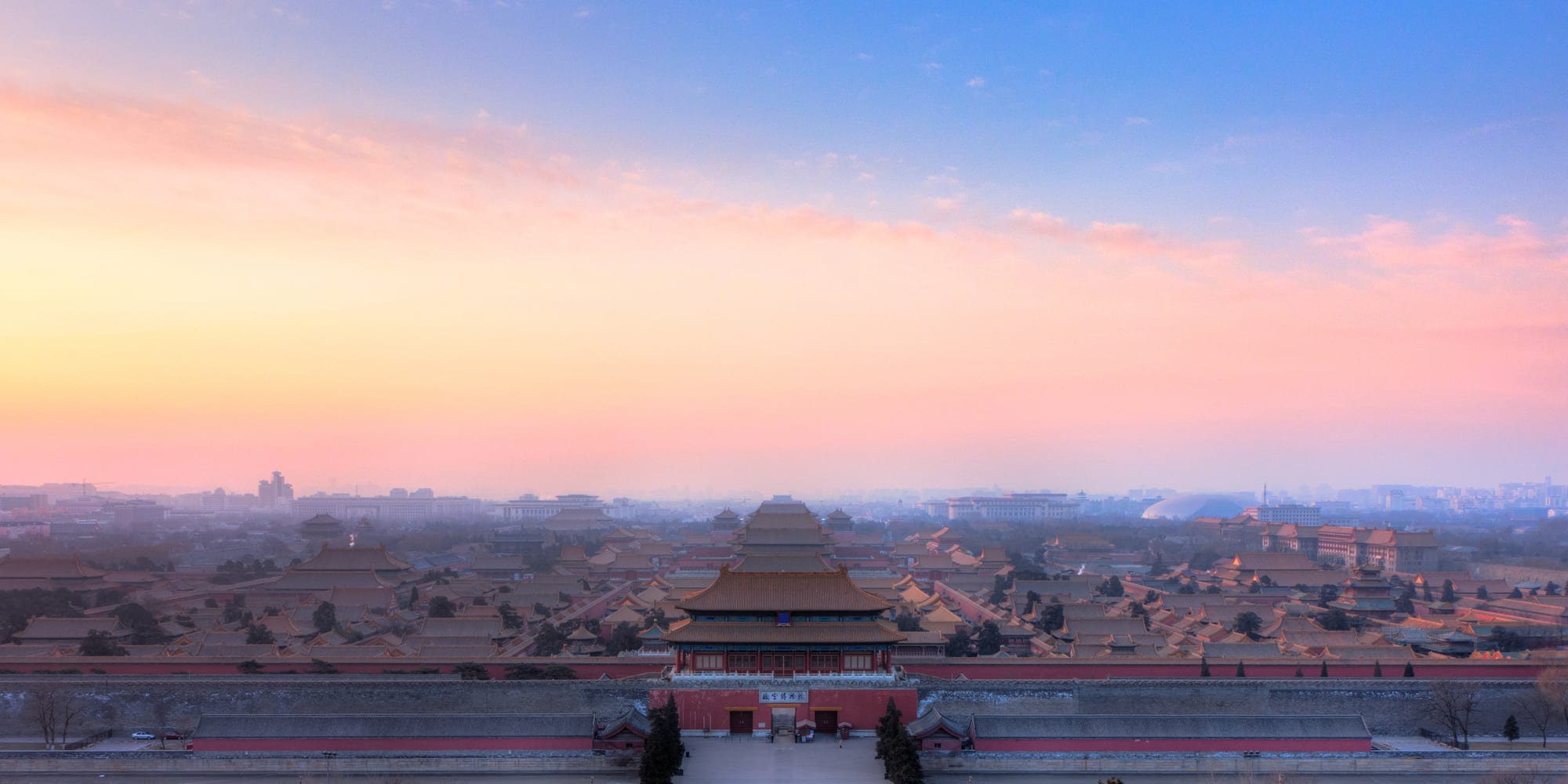 A vast walled palace complex of golden-roofed halls and courtyards seen from a hill, with a city beyond