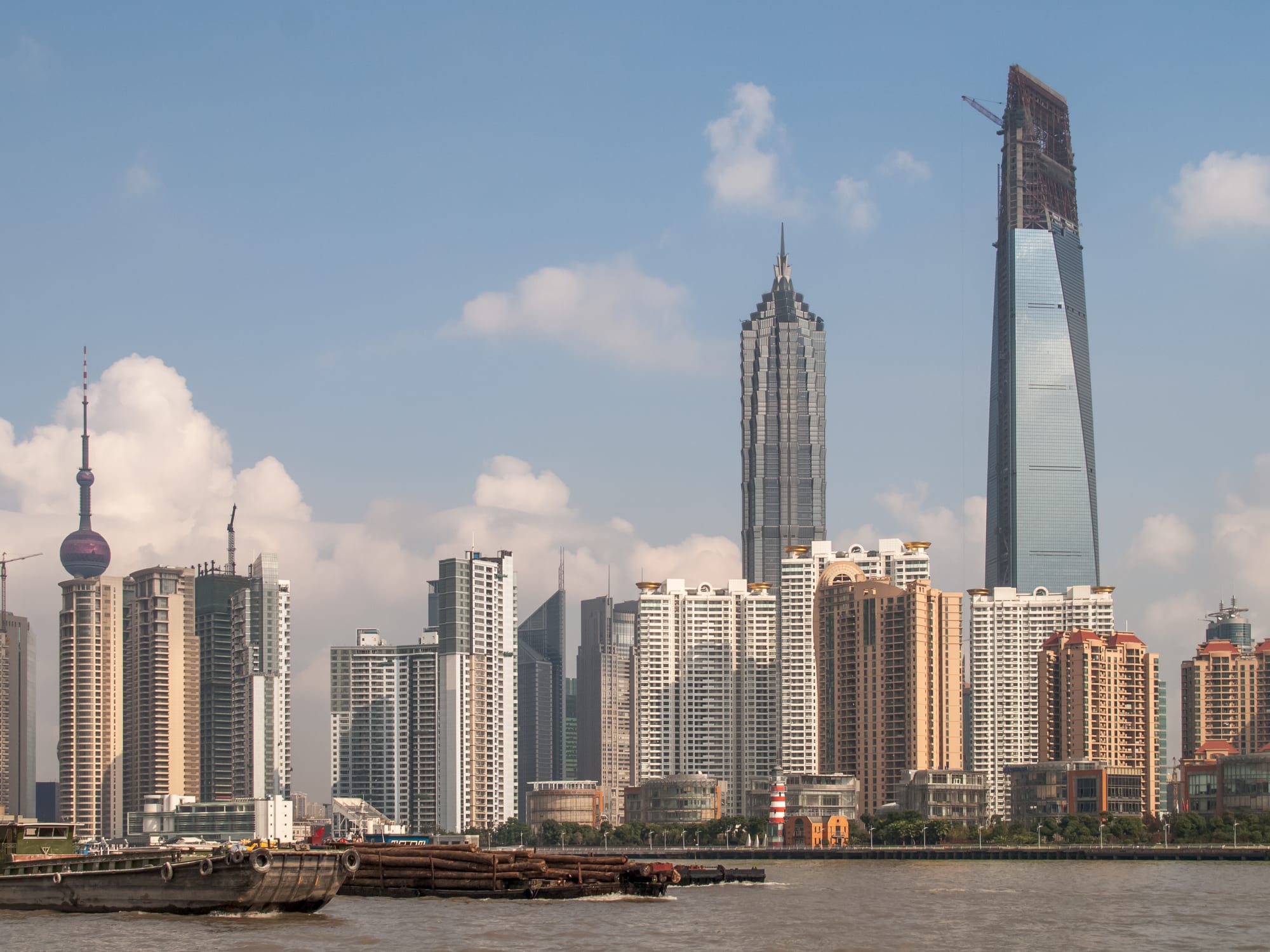 A dense cluster of supertall skyscrapers along a river bend, seen across the water at dusk