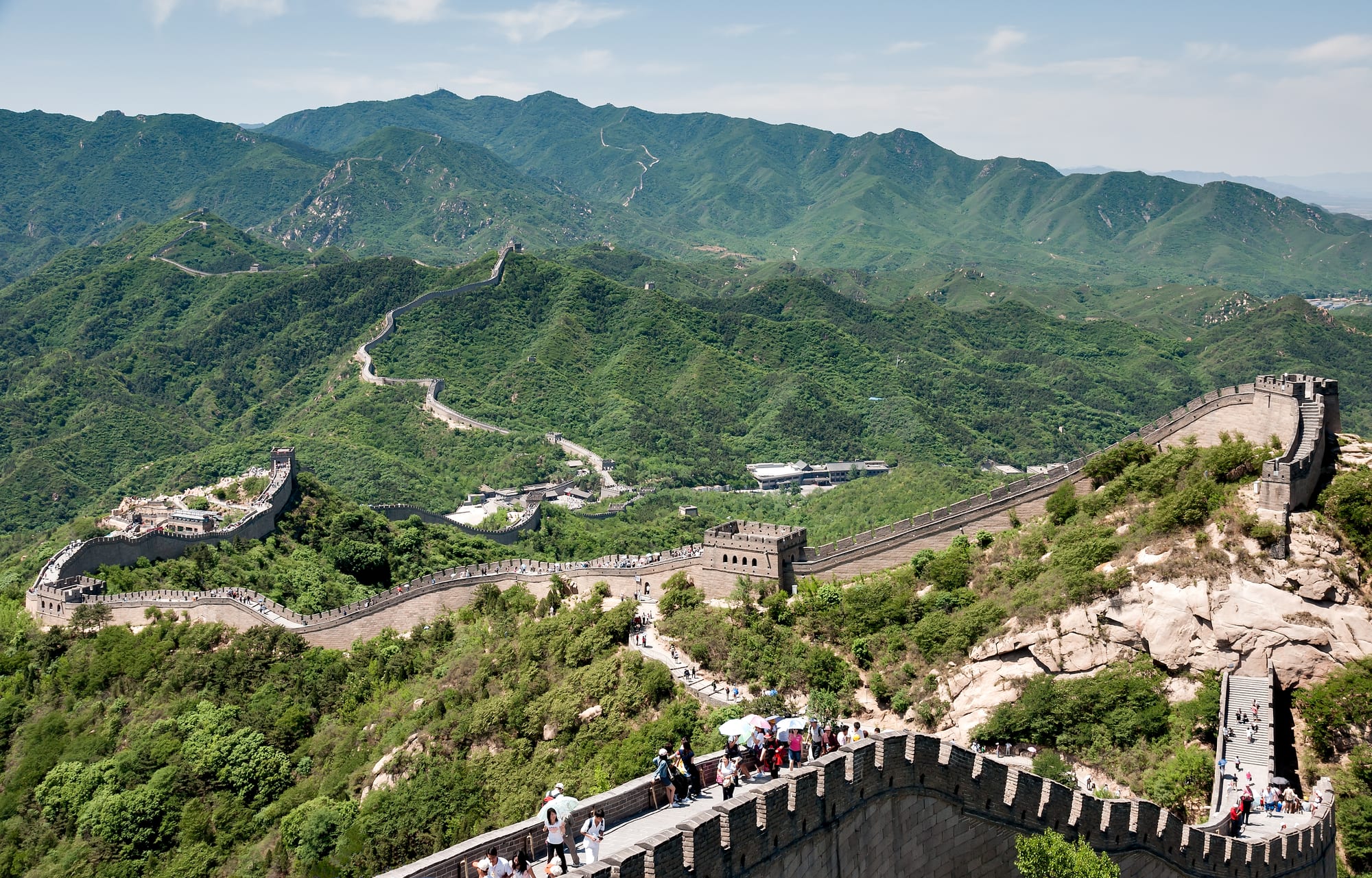 A stone wall with watchtowers snaking along the crests of steep green mountain ridges into the distance