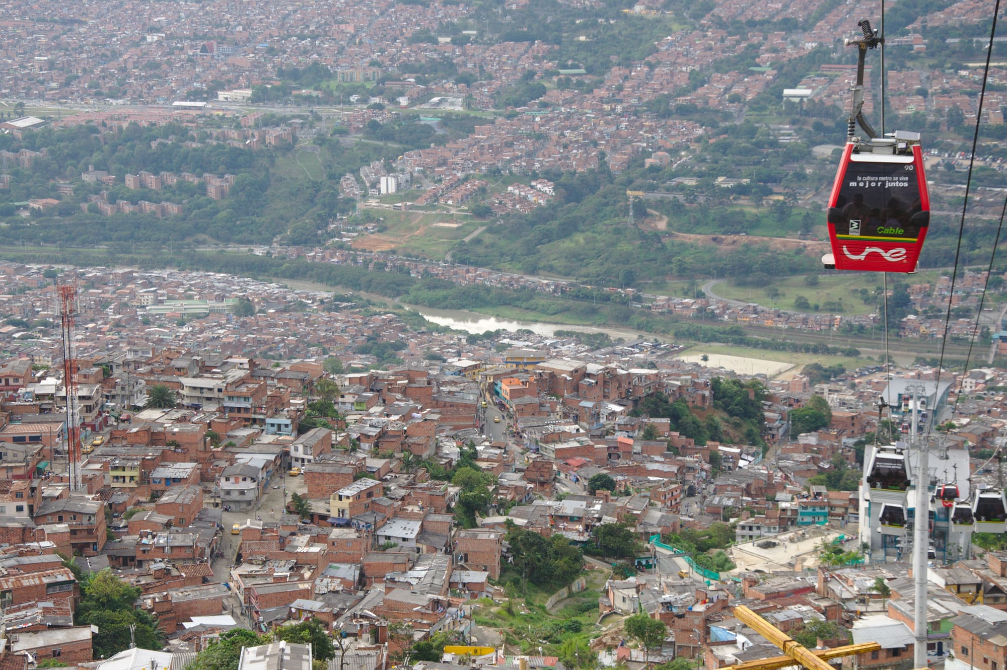 A cable car gondola in the foreground with a dense hillside neighbourhood of brick houses spreading across a valley below