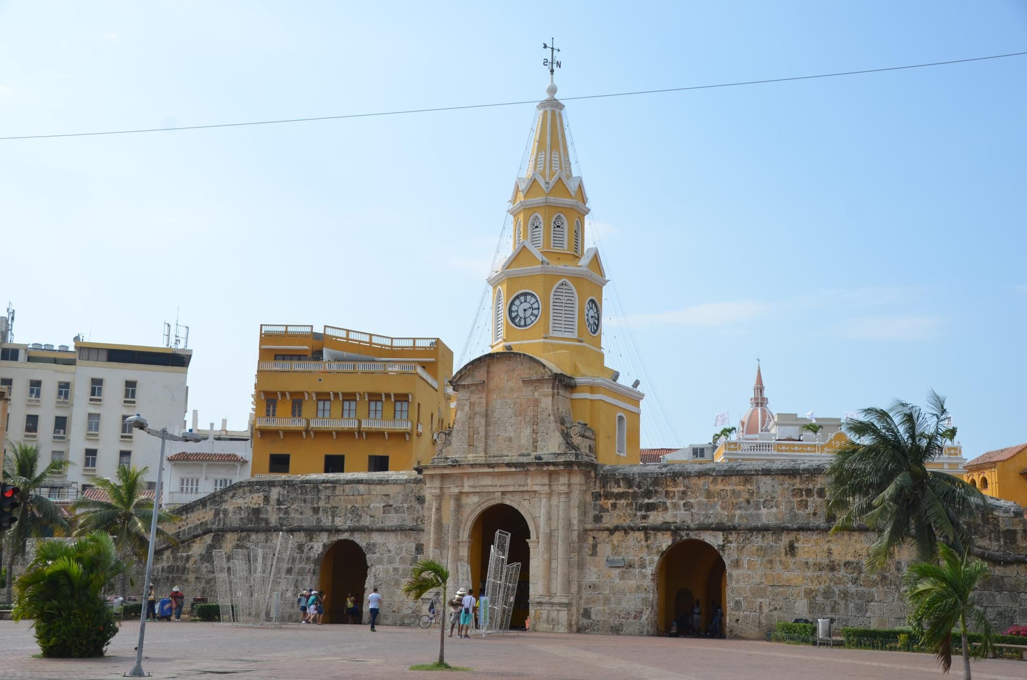 A yellow colonial clock-tower gate set in massive stone city walls, palms in front