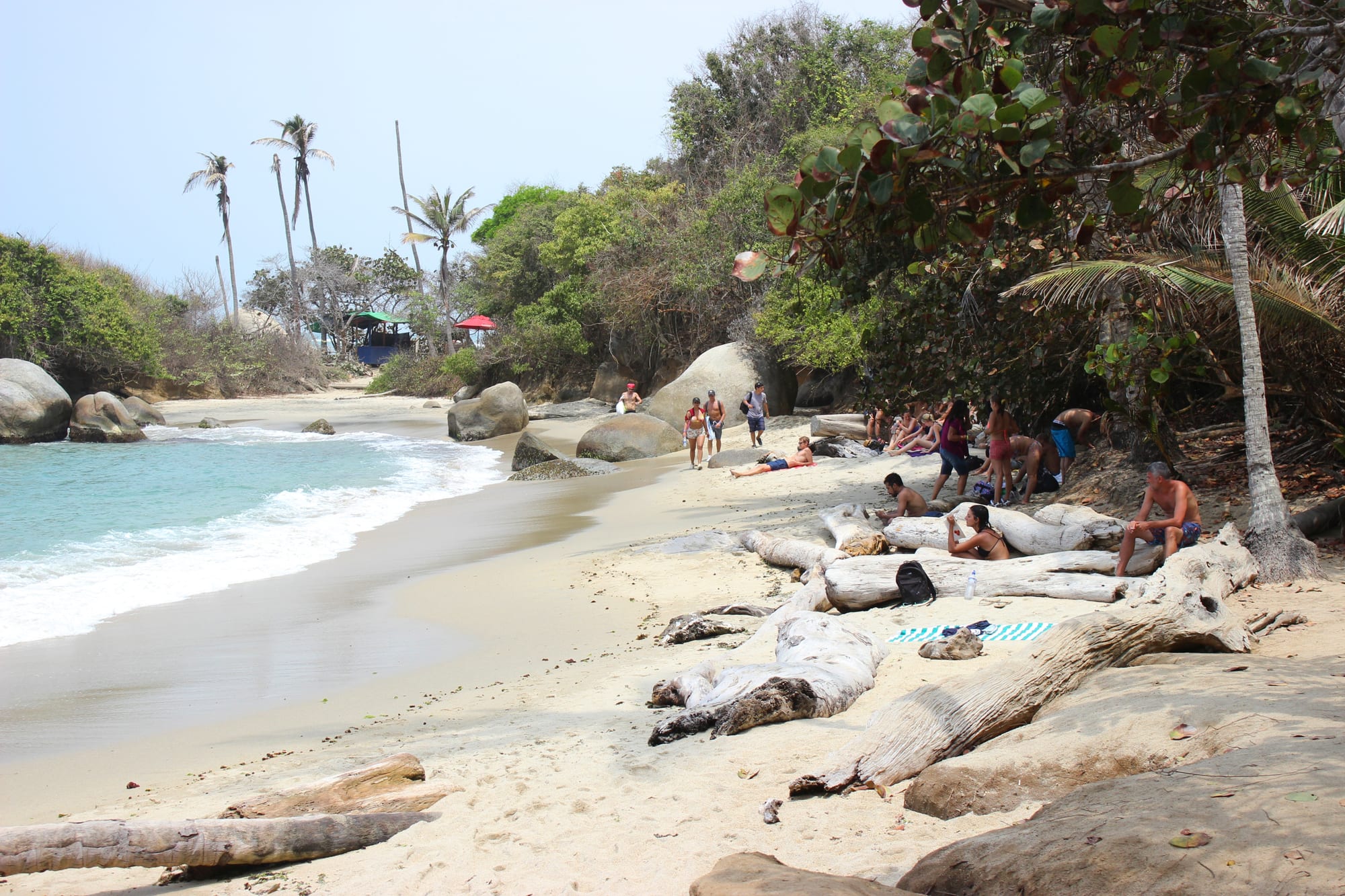 A double cove of golden sand and a rocky headland topped by a thatched hut, jungle behind
