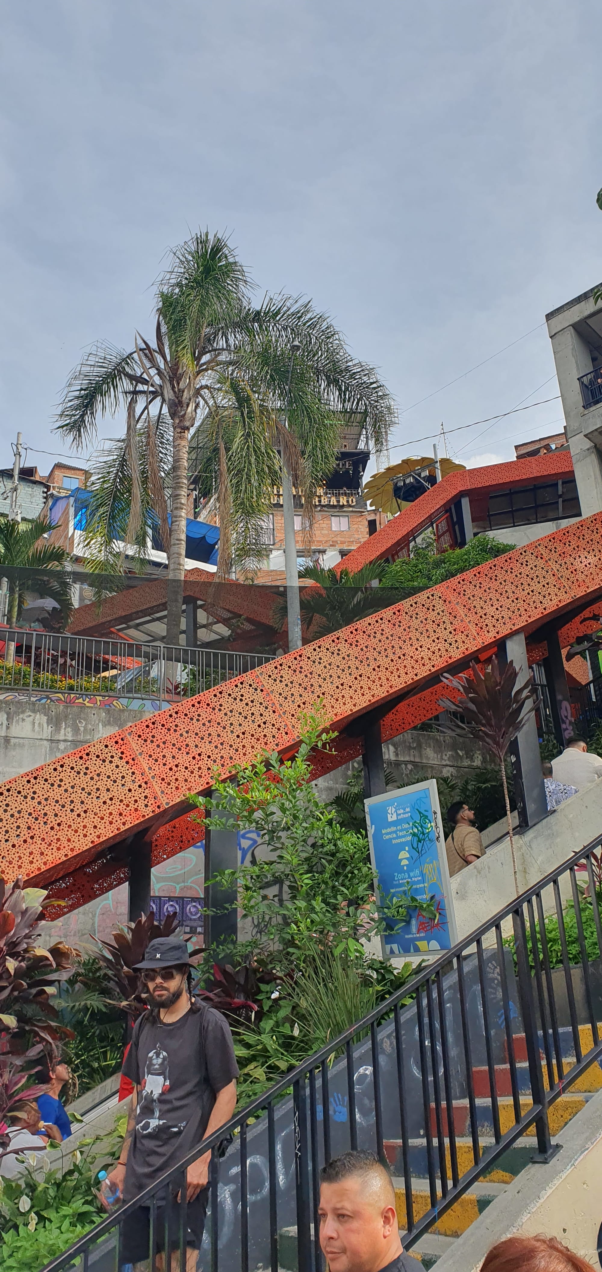 Outdoor covered escalators climbing a steep hillside of brick houses covered in murals