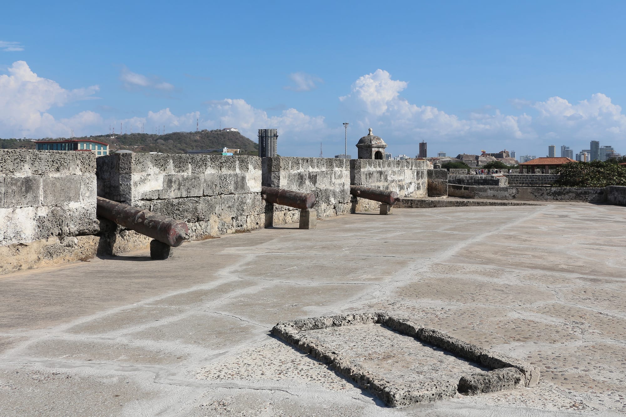 Thick sloping stone ramparts with sentry boxes running along a seafront beside a modern city