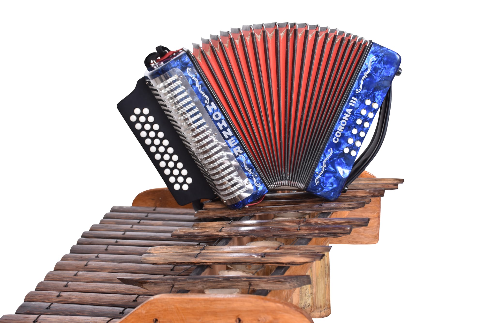 A red and blue button accordion resting on top of a wooden marimba with dark wooden keys, photographed against a white background